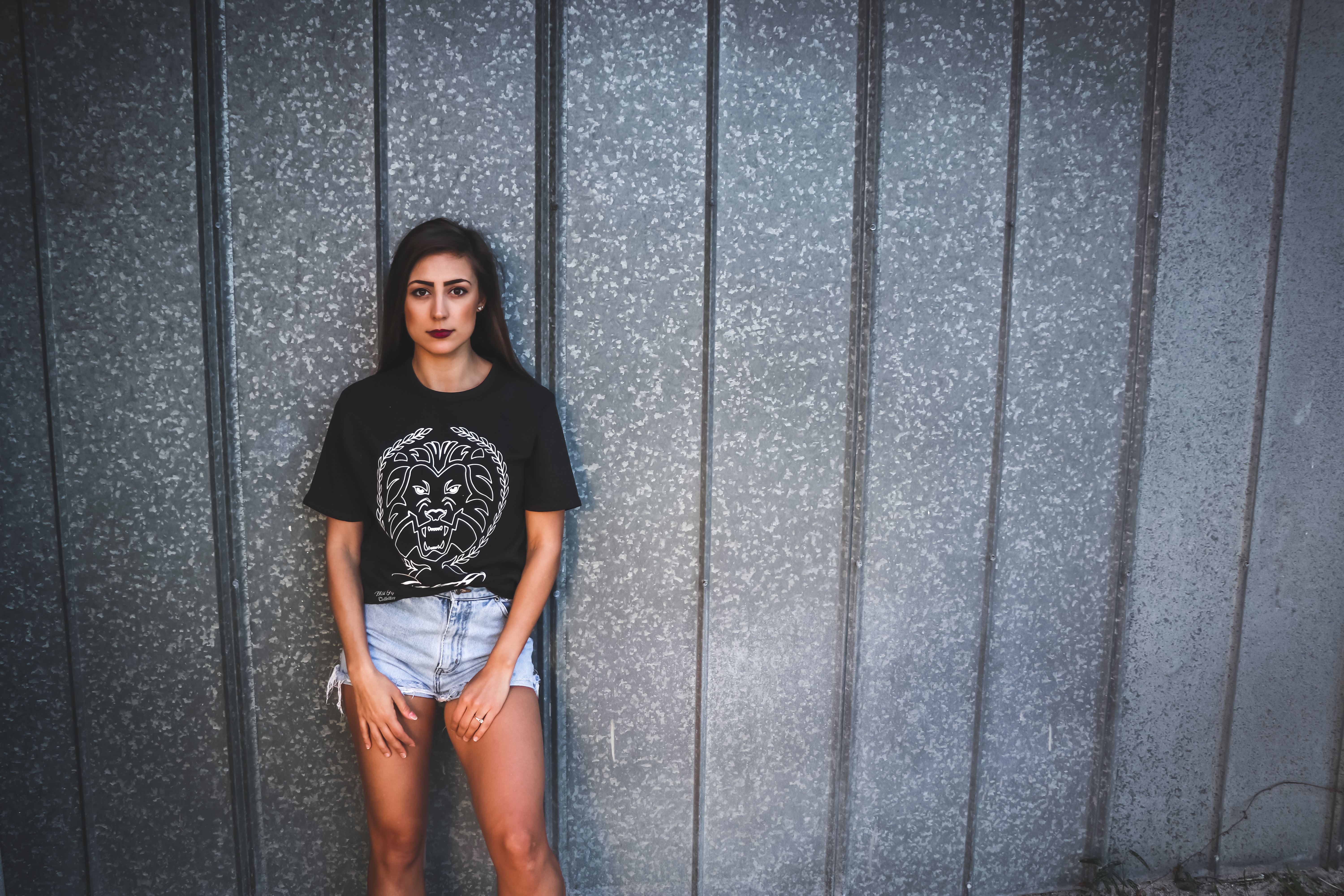Woman wearing black lion graphic crew-neck shirt and gray denim short shorts leaning on gray wall photo