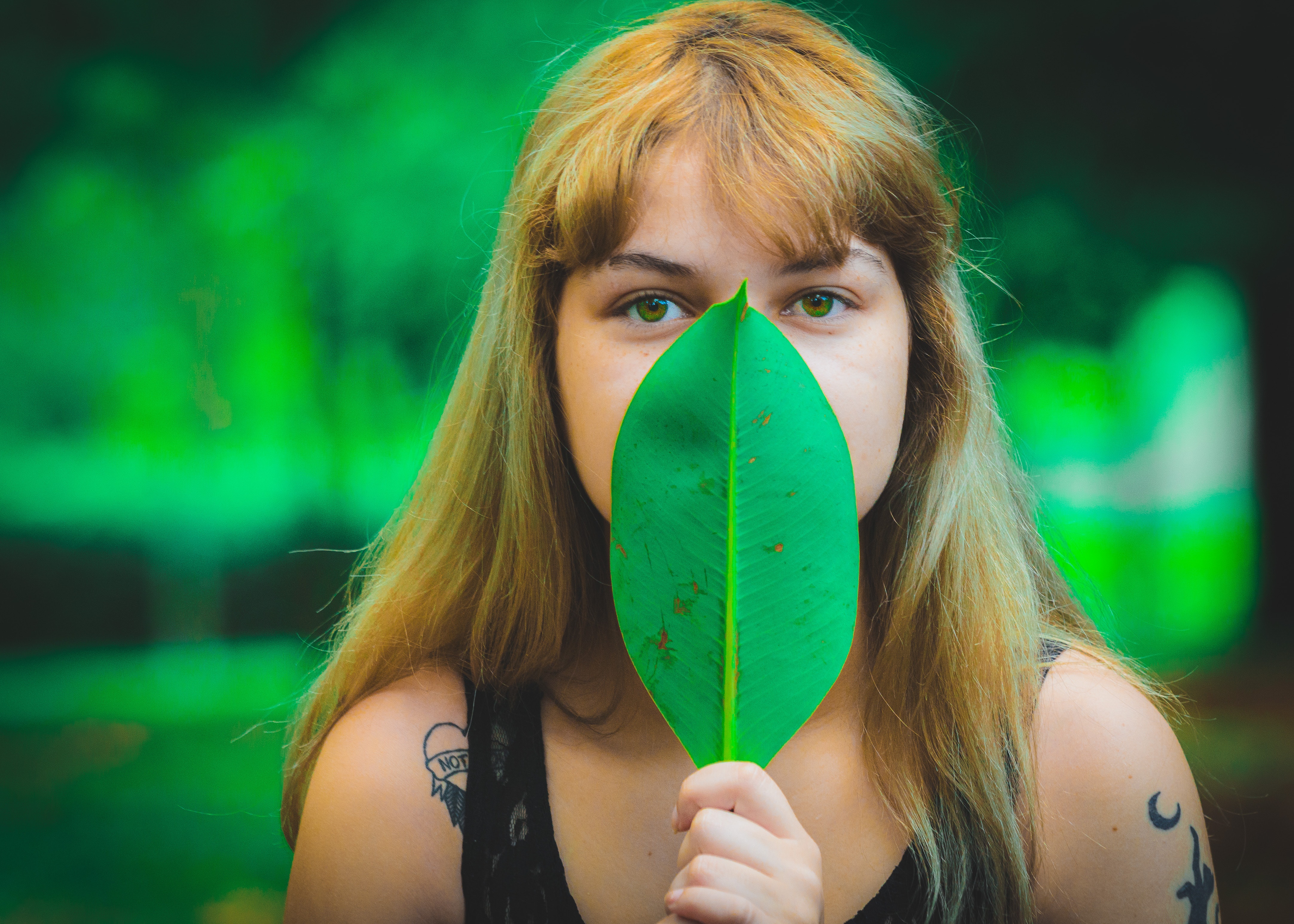 Woman wearing black sleeveless top covering mouth using green leaf photo