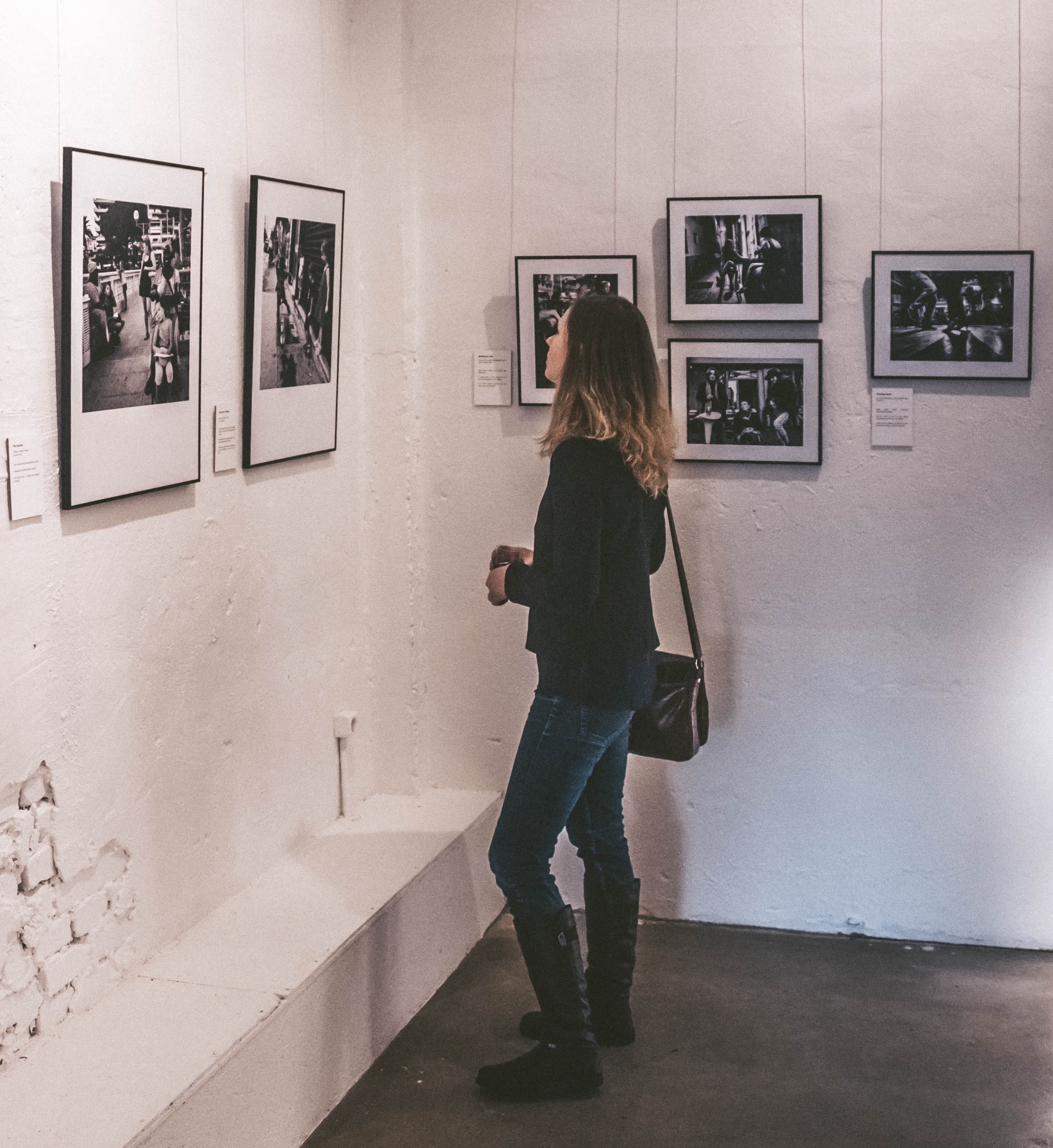 Woman wearing black sweater and blue denim jeans staring at paintings inside well-lit room photo