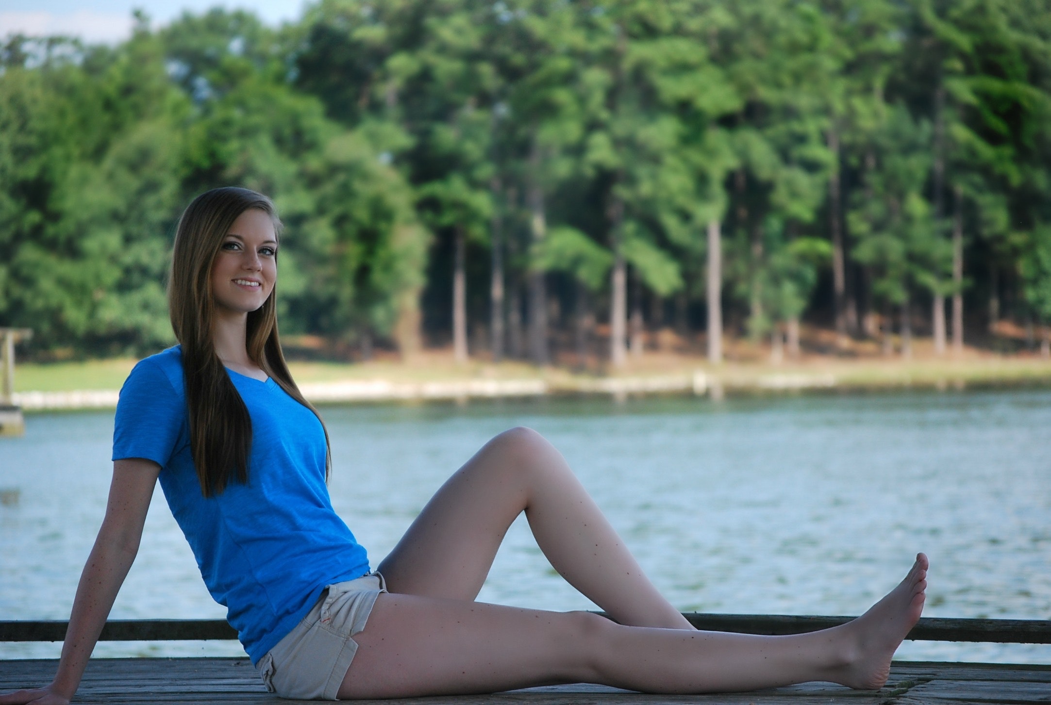 Woman wearing blue t shirt and beige short sitting on brown wooden panel near body of water during daytime photo