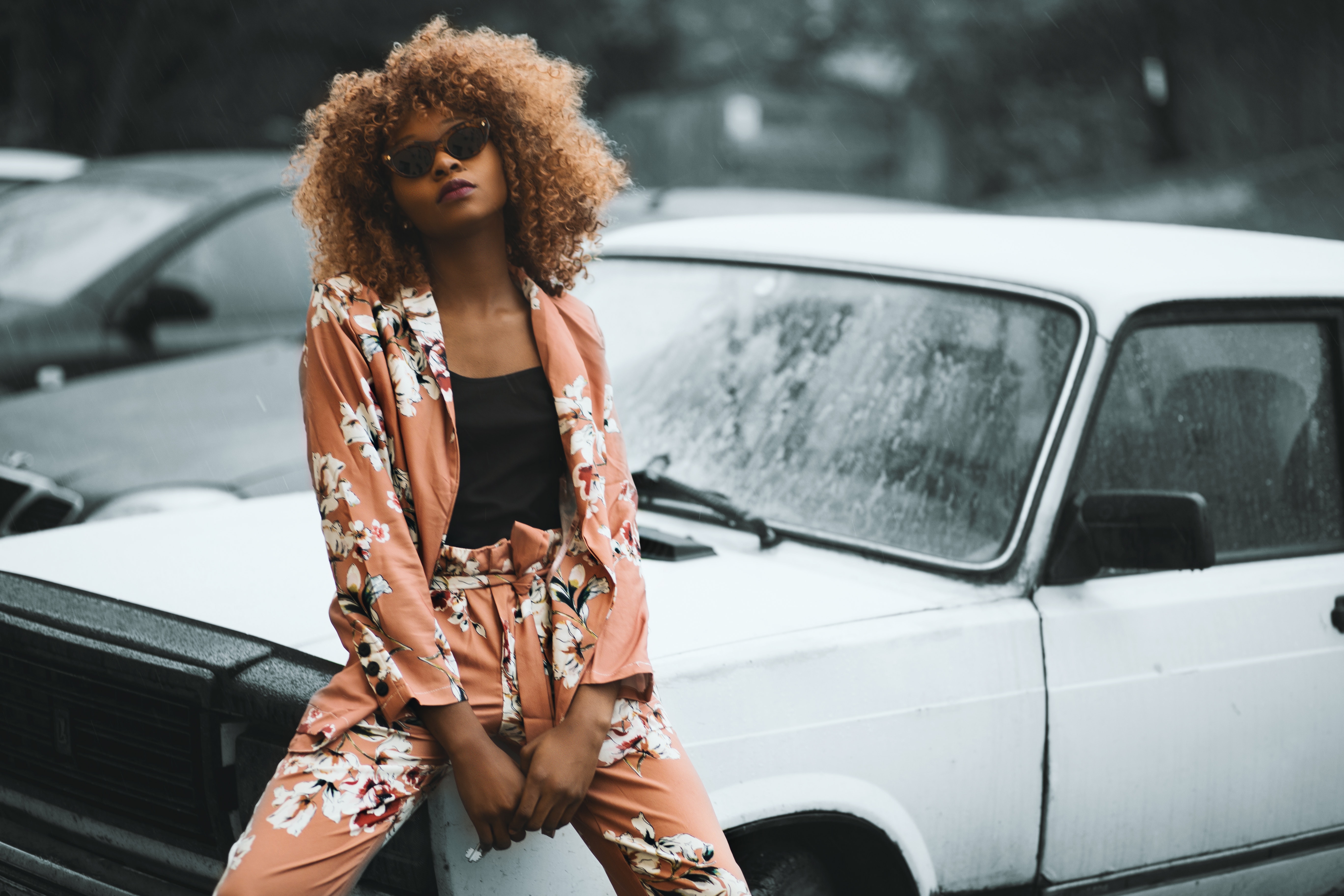 Woman wearing brown floral print coat and pants sitting on car photo