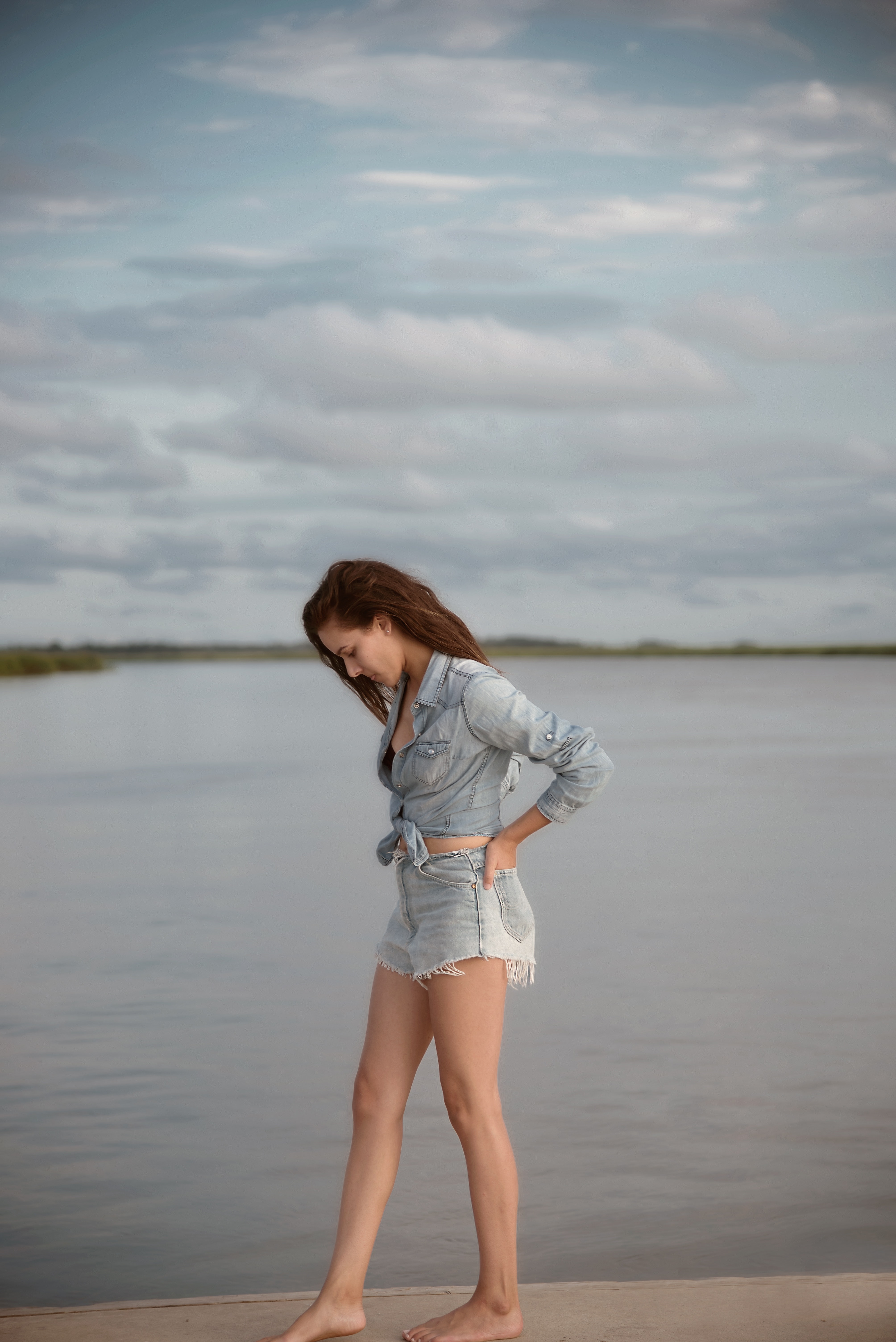Woman wearing gray denim tie-front long-sleeved shirt and short shorts walking on isle near body of water photo
