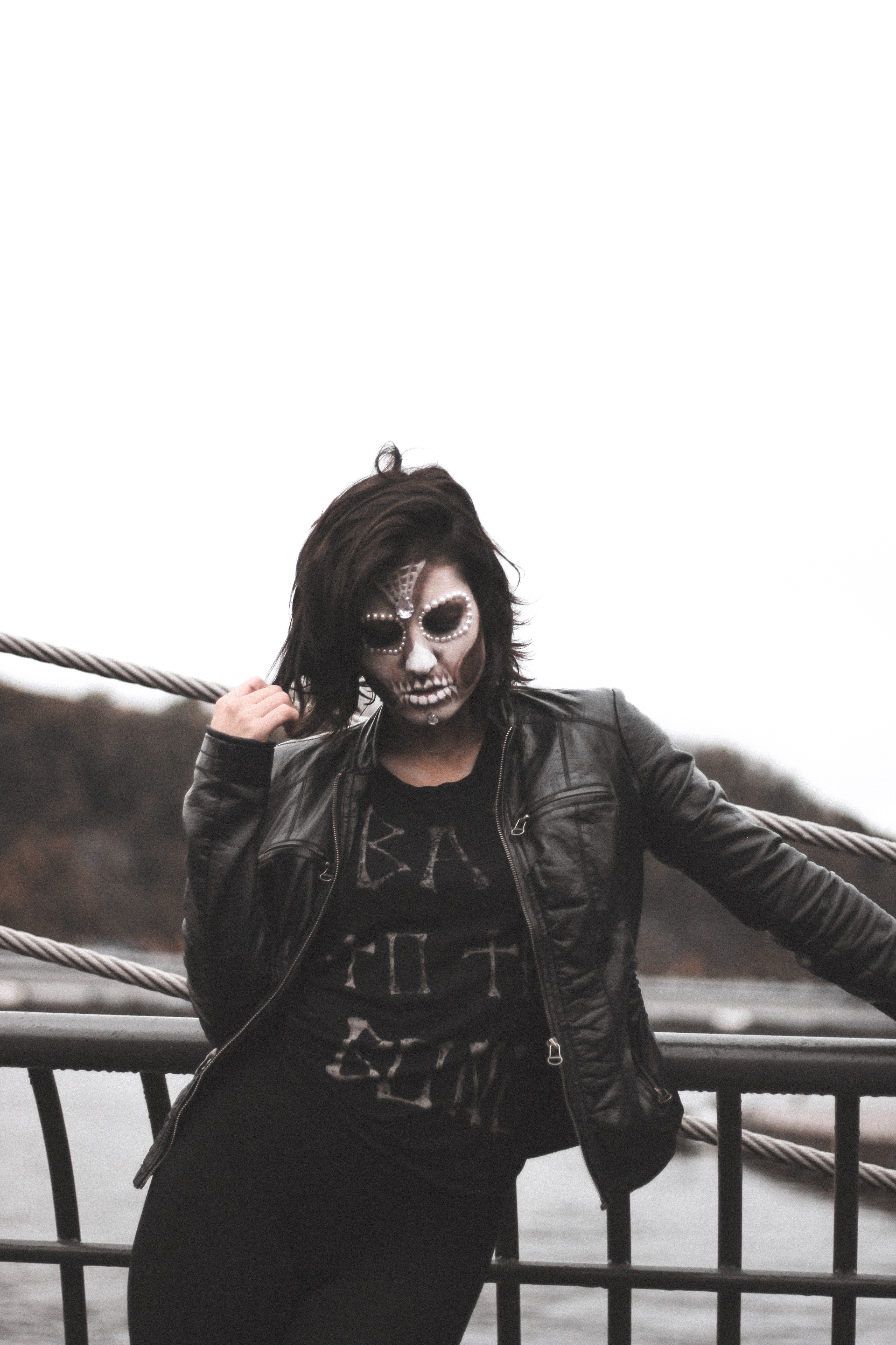 Woman wearing gray halloween mask and black leather jacket standing by black railings photo