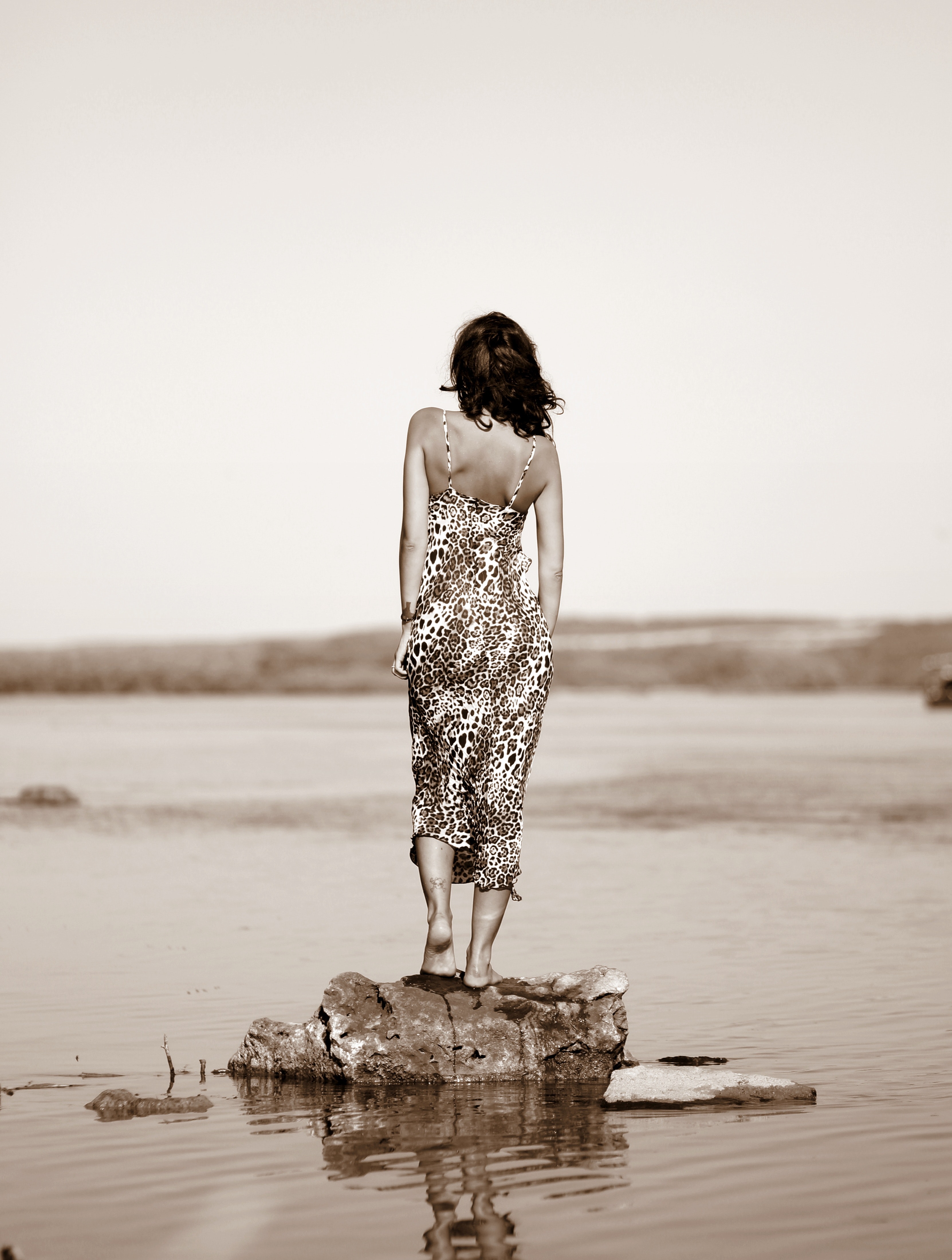 Woman wearing leopard print dress standing on stone on body of water photo