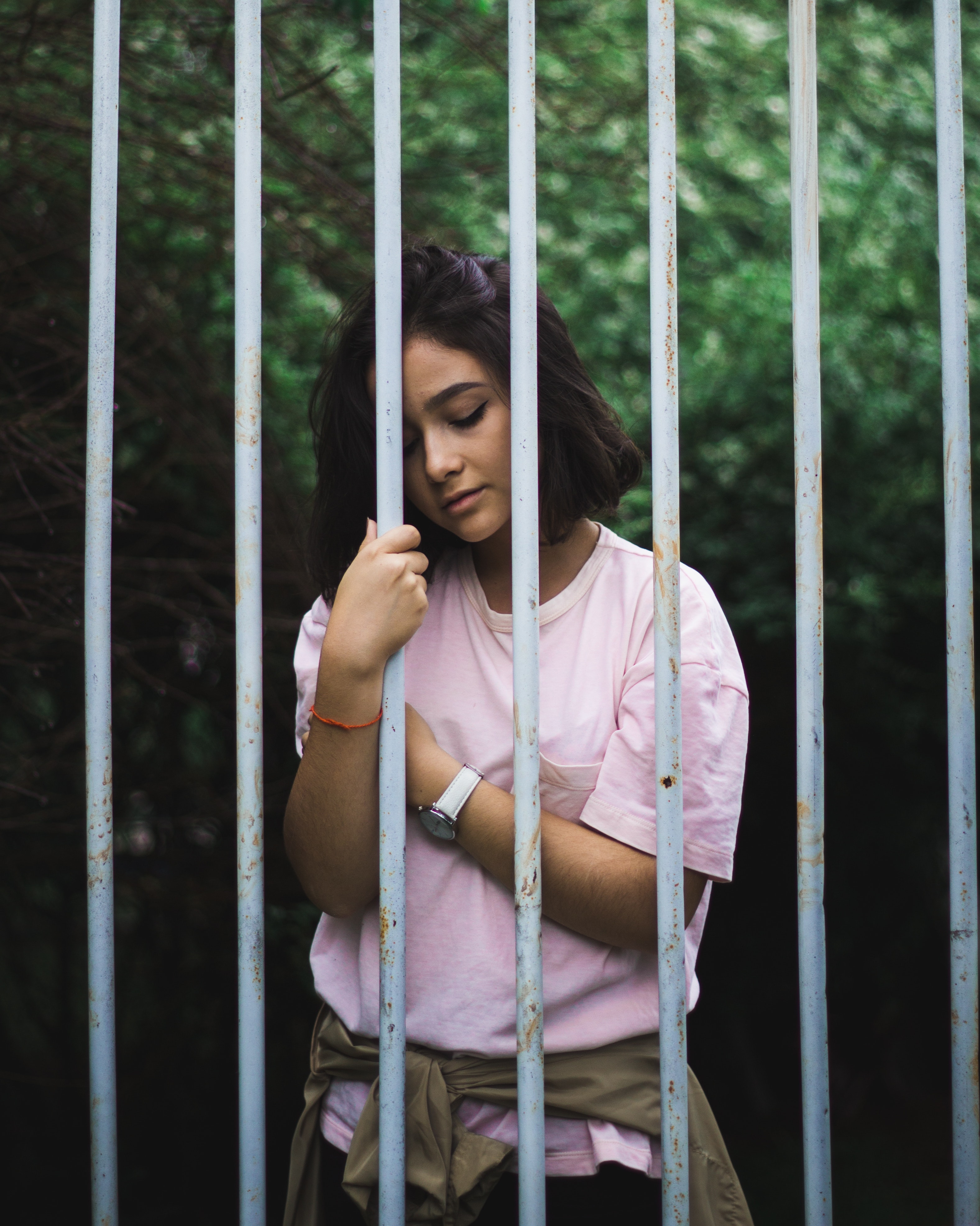 Woman wearing pink crew-neck t-shirt standing and leaning behind white bars photo