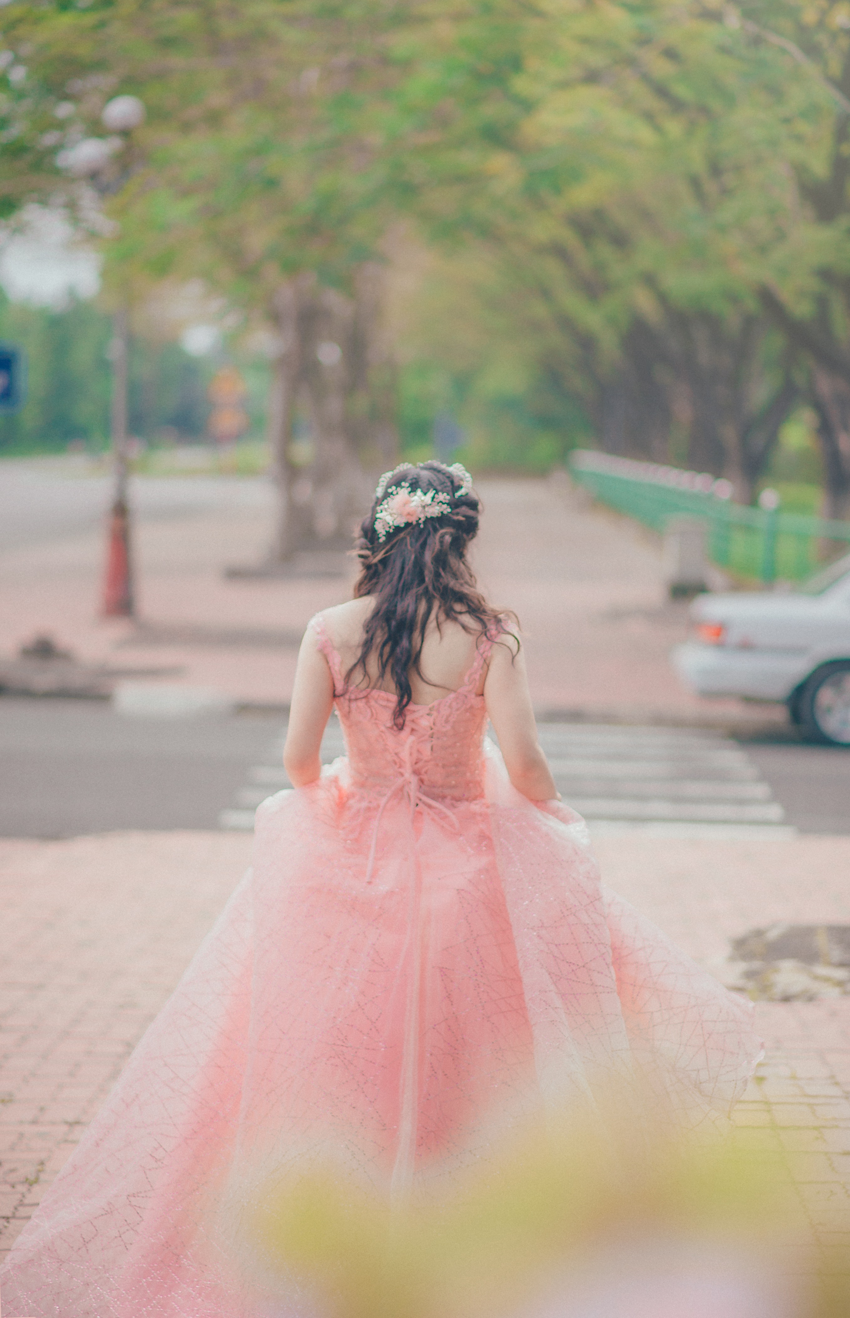 Woman wearing pink floral gown stands near green trees at daytime photo
