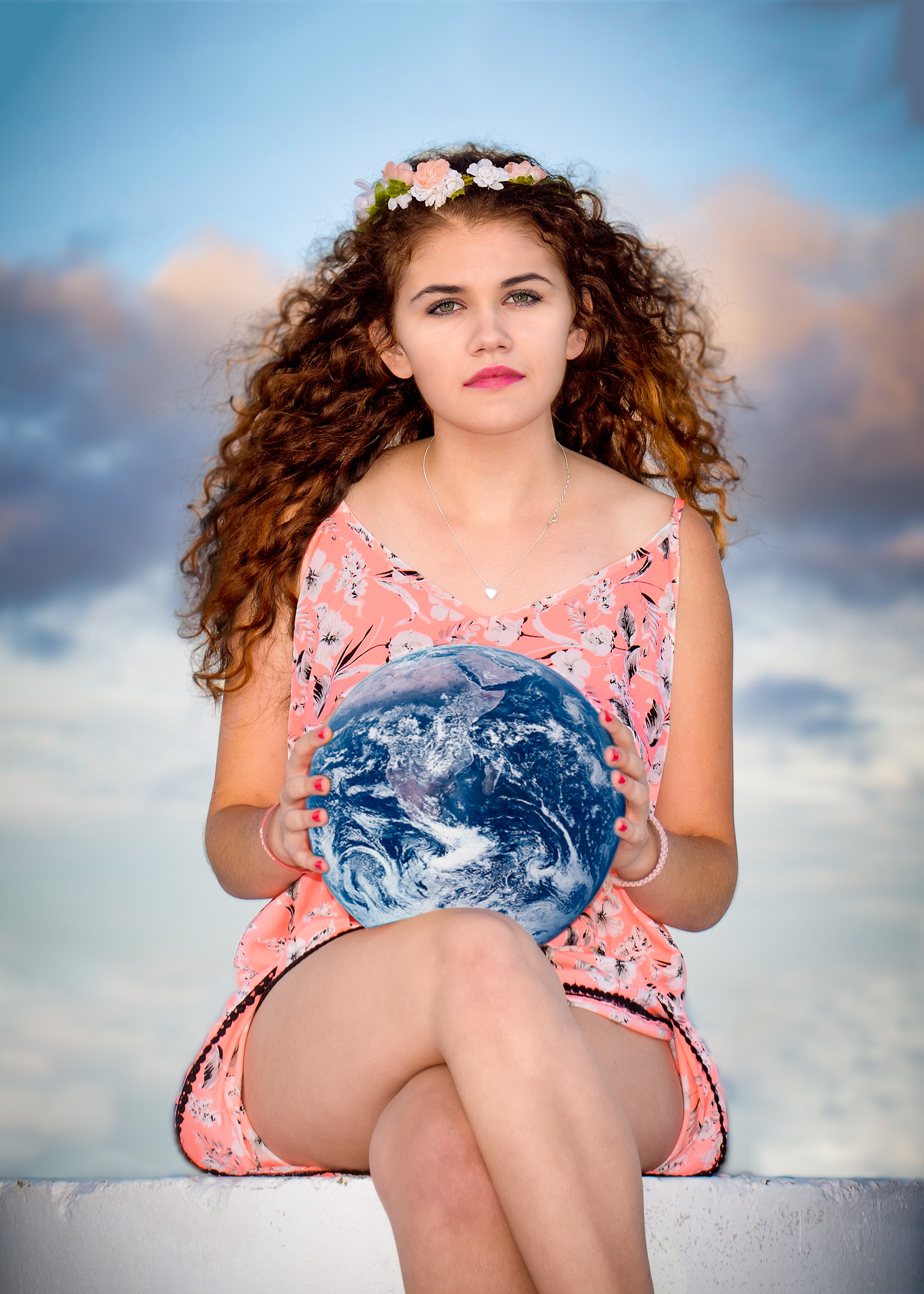 Woman wearing pink floral sleeveless romper sitting on gray concrete holding earth globe photo