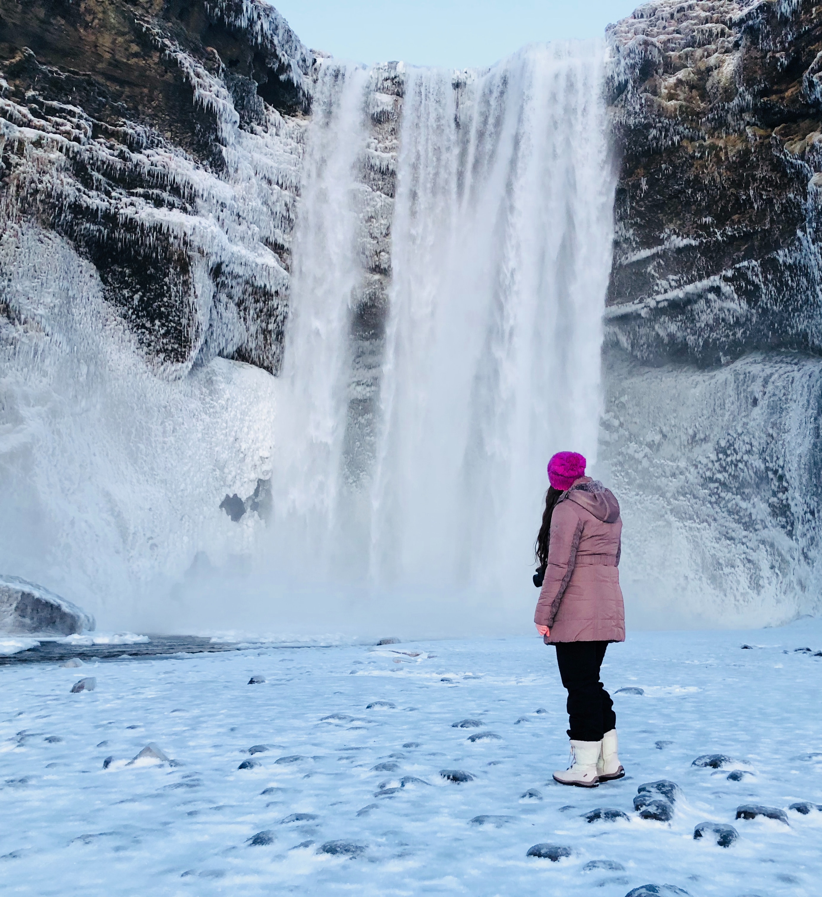 Woman wearing pink snow coat standing on field full of snow in front of frozen waterfalls photo