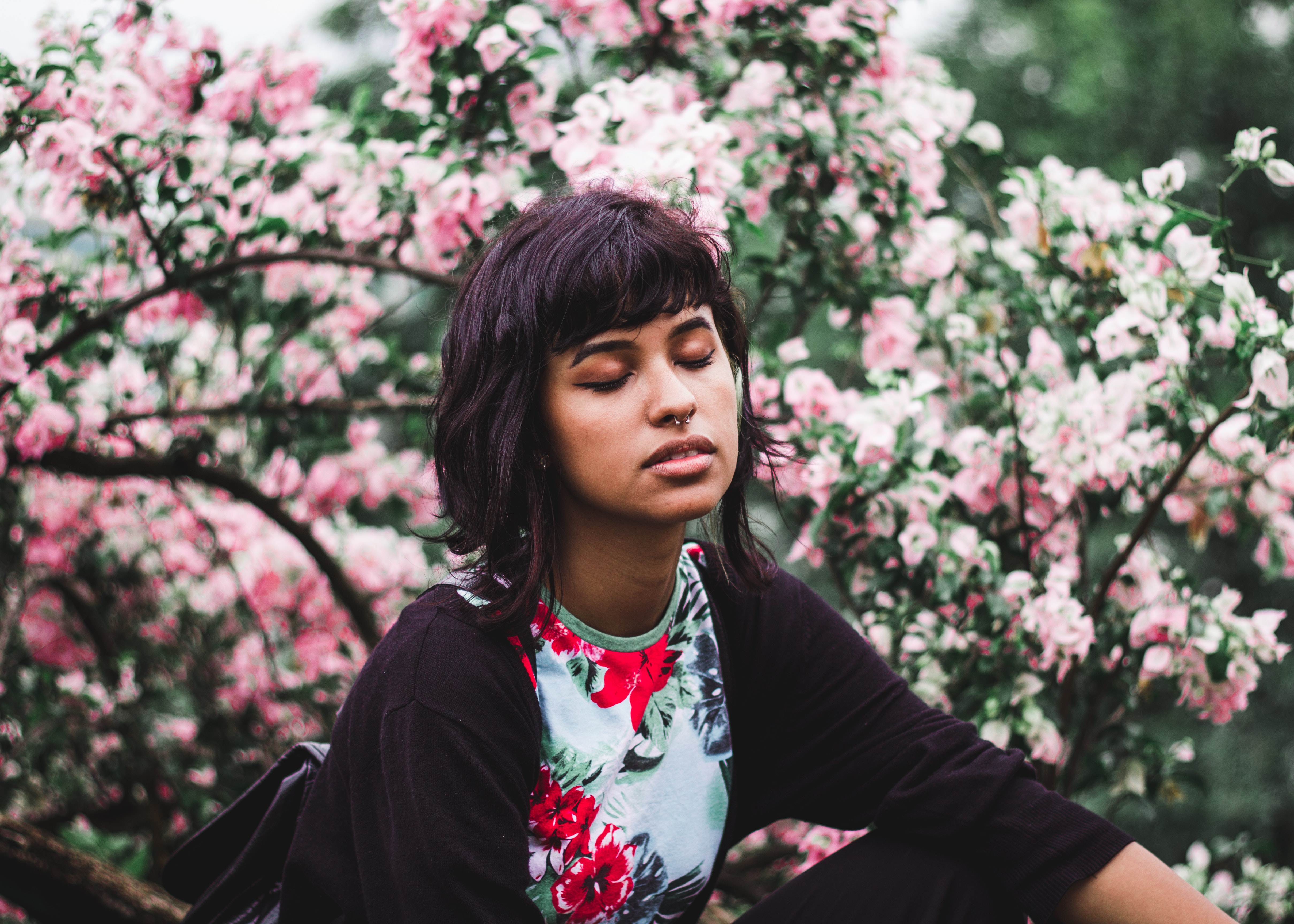 Woman wearing white and red floral crew-neck shirt near pink petaled plant photo