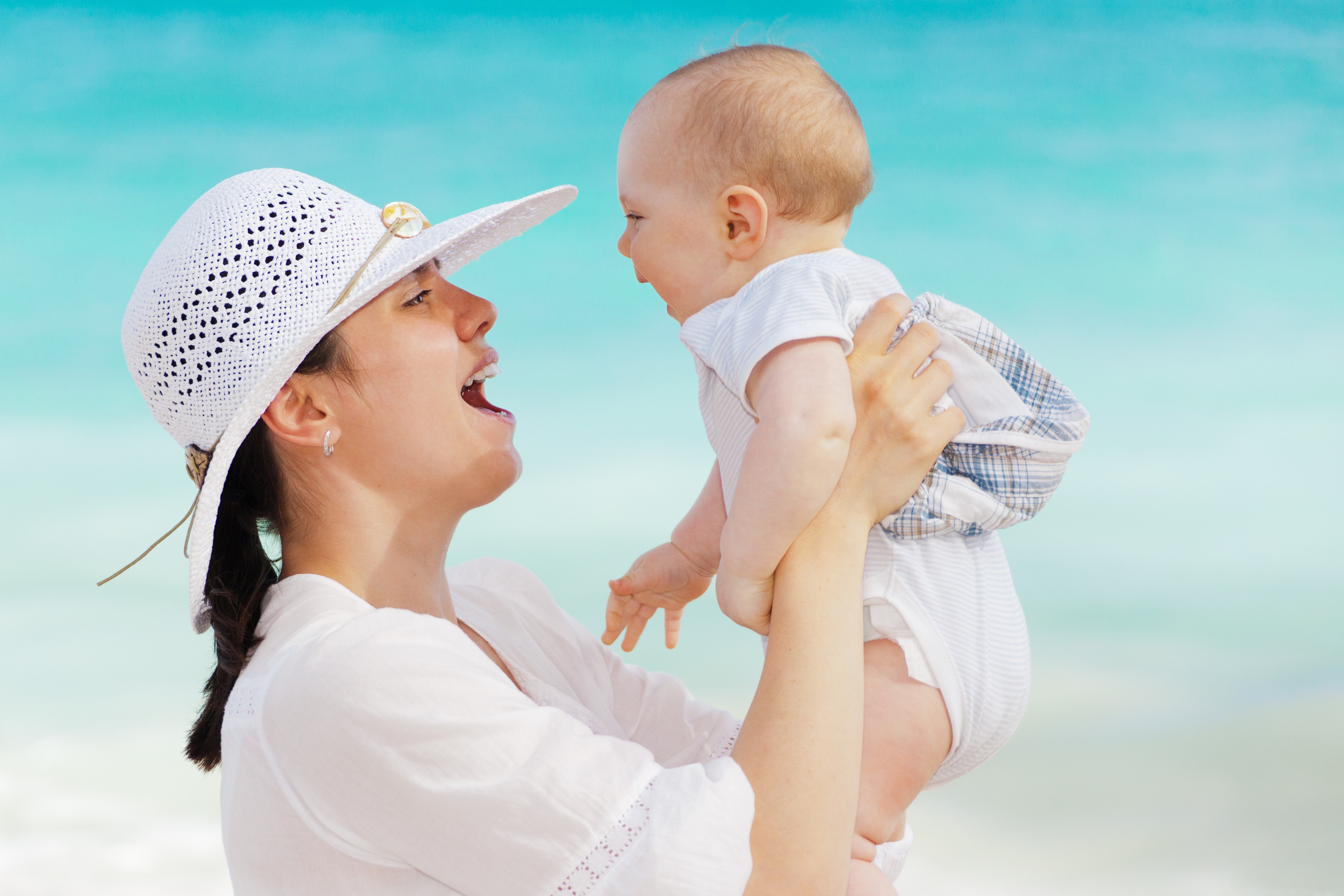 Woman wearing white hat holding baby wearing white onesie near beach during day time photo