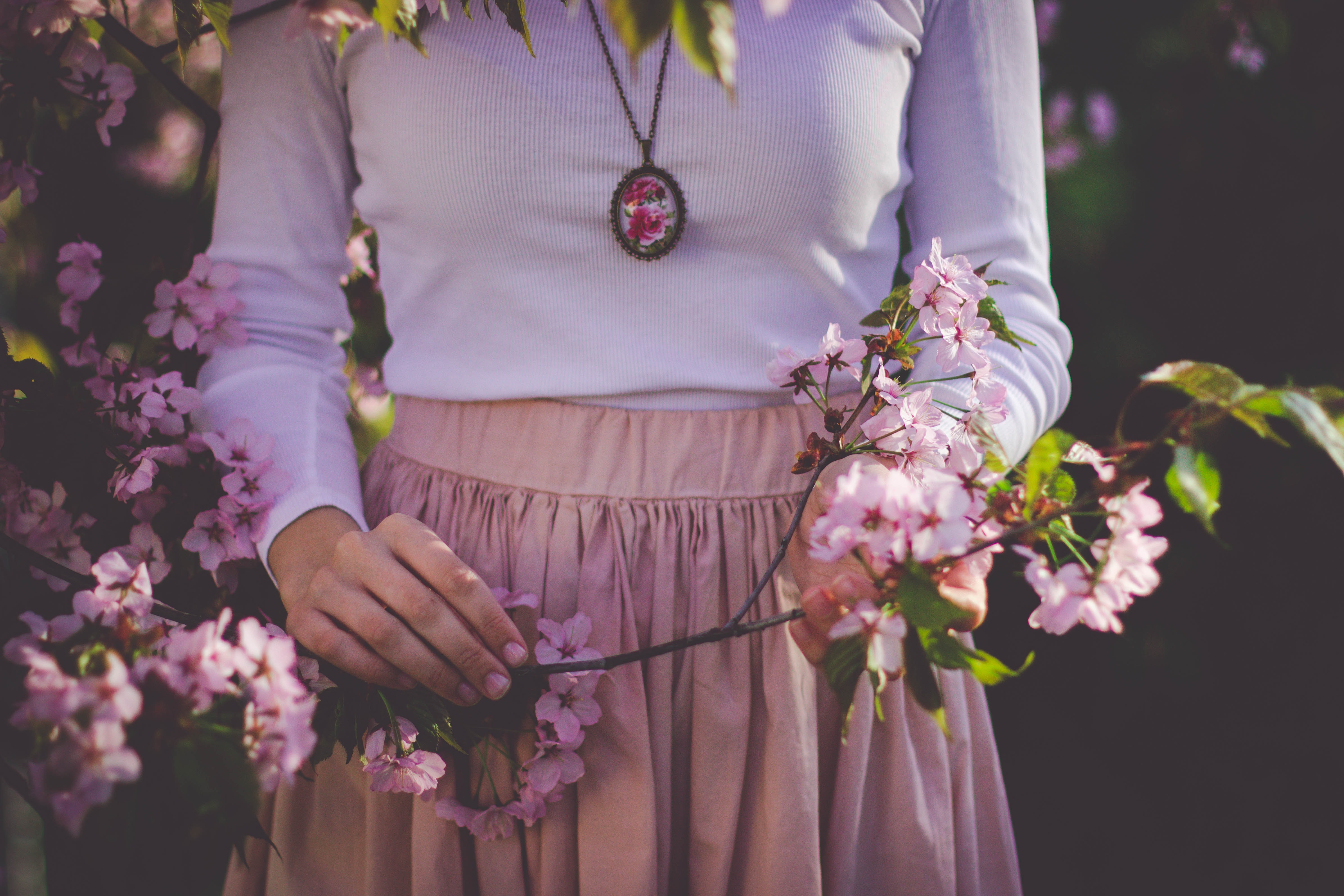 Woman wearing white long sleeve shirt and beige skirt holding pink petaled flower photo