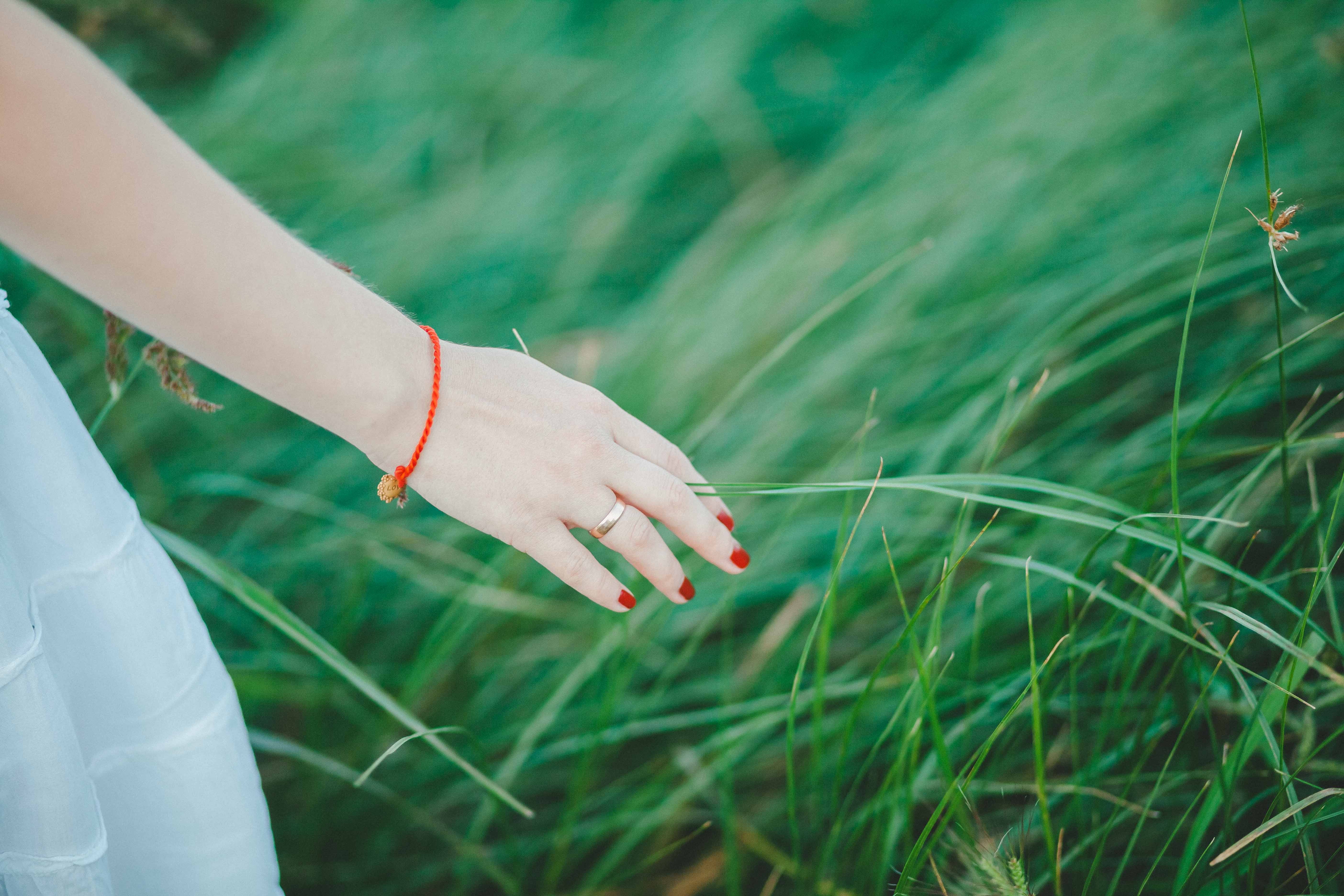 Woman wearing white skirt, orange bracelet, and red manicure beside green grass photo