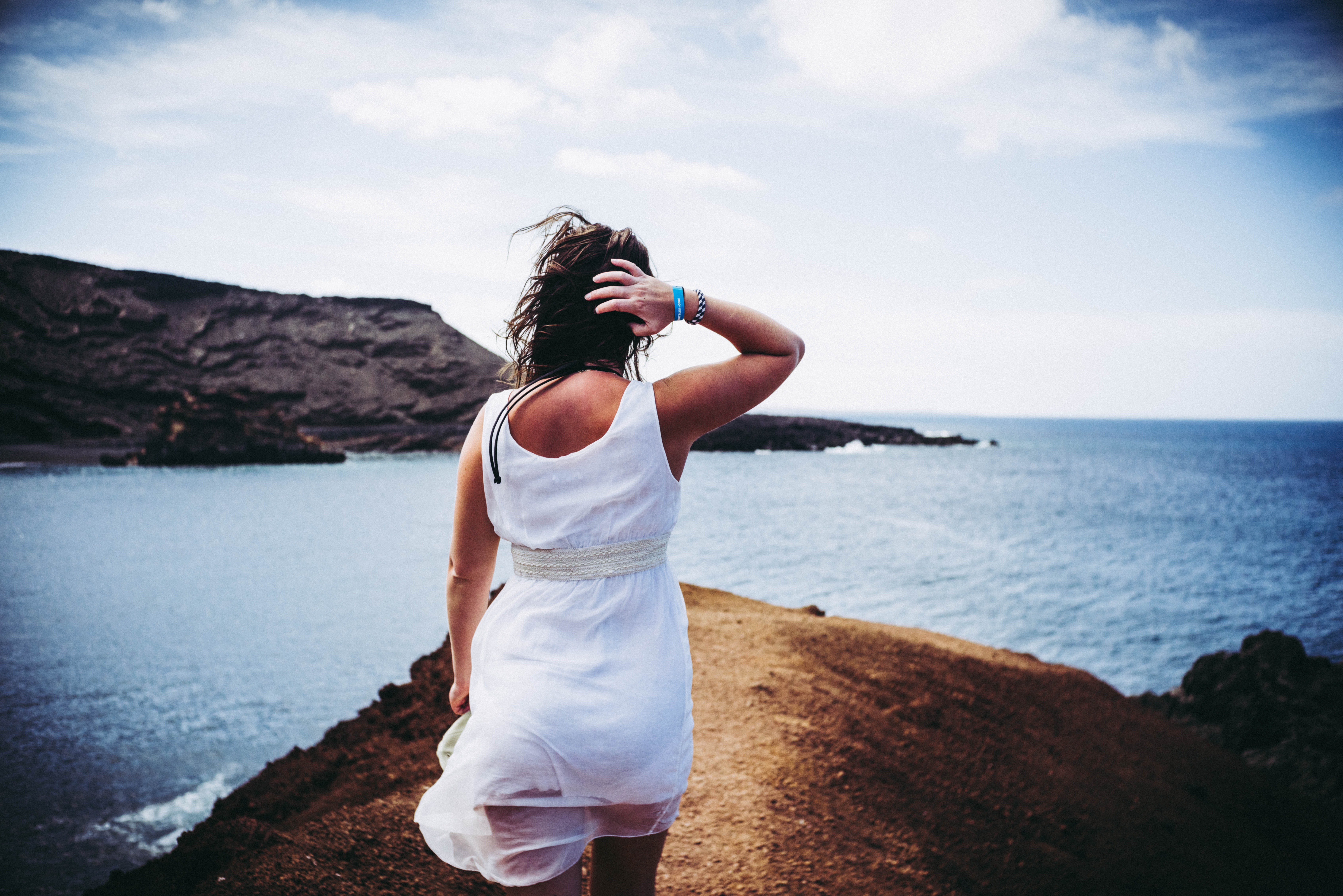 Woman wearing white sleeveless mini dress on top of brown sand near body of water photo