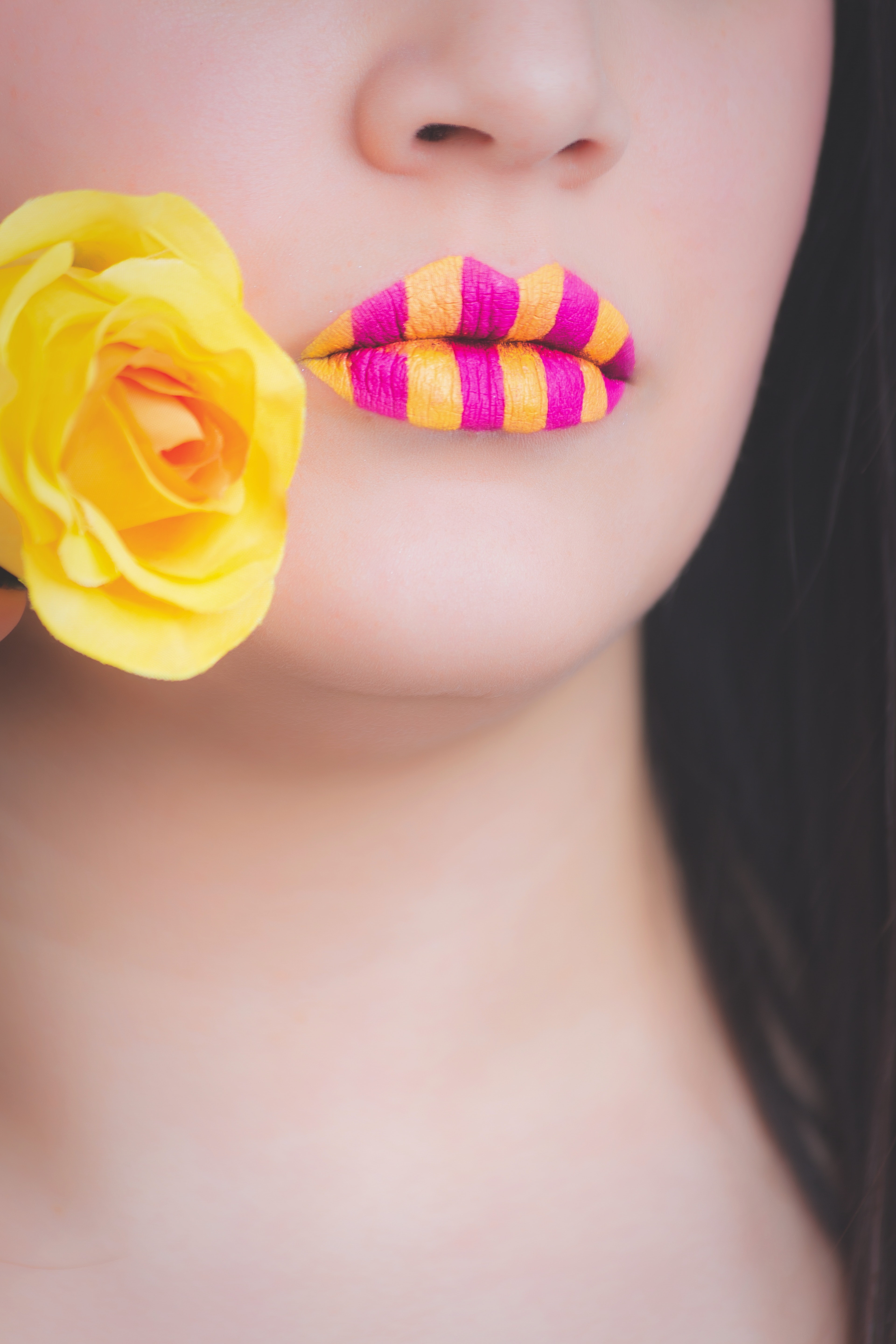 Woman wearing yellow and pink striped lipstick holding yellow rose photo