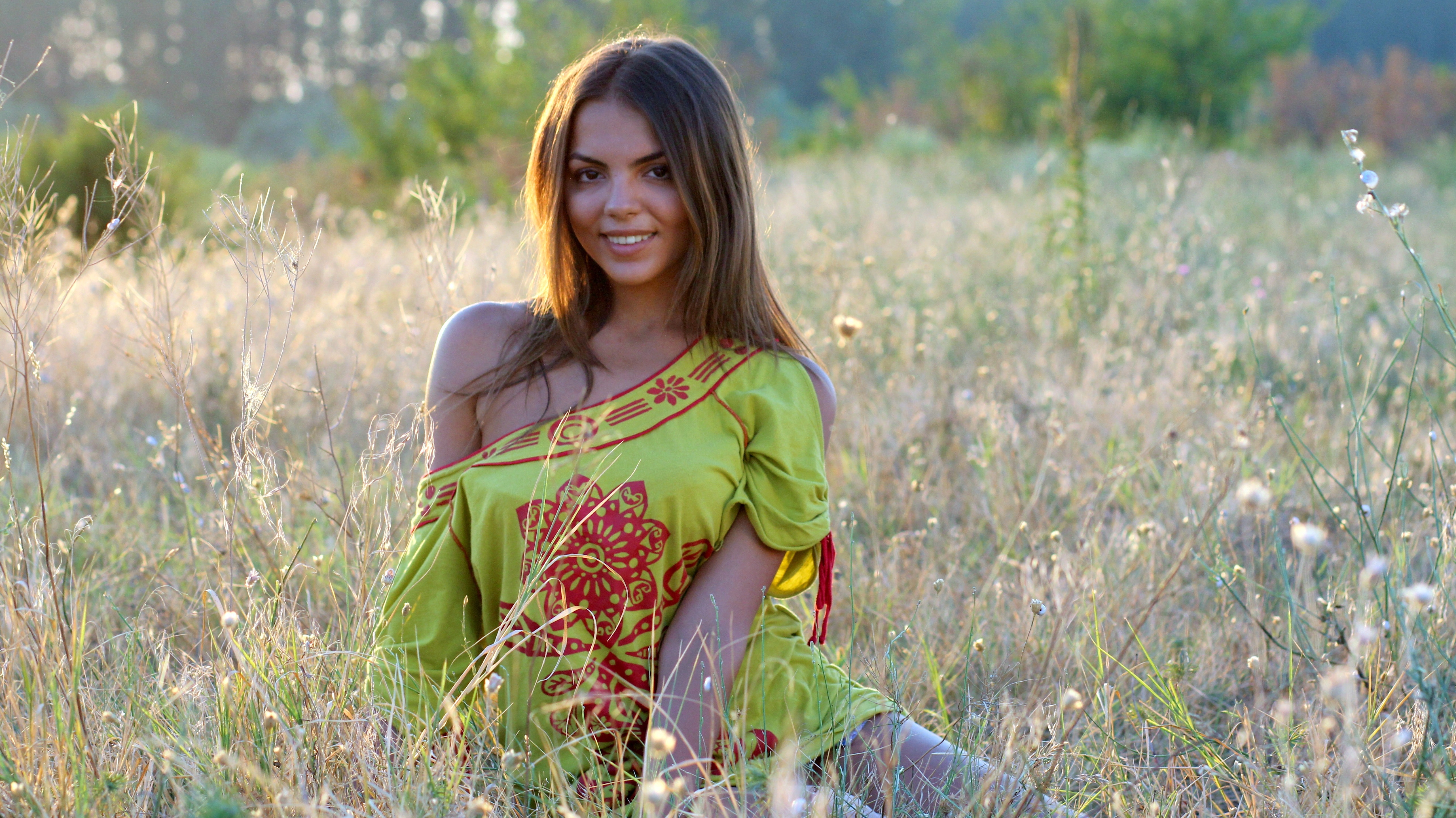Woman wearing yellow and red dress sitting on the ground while looking at the camera photo