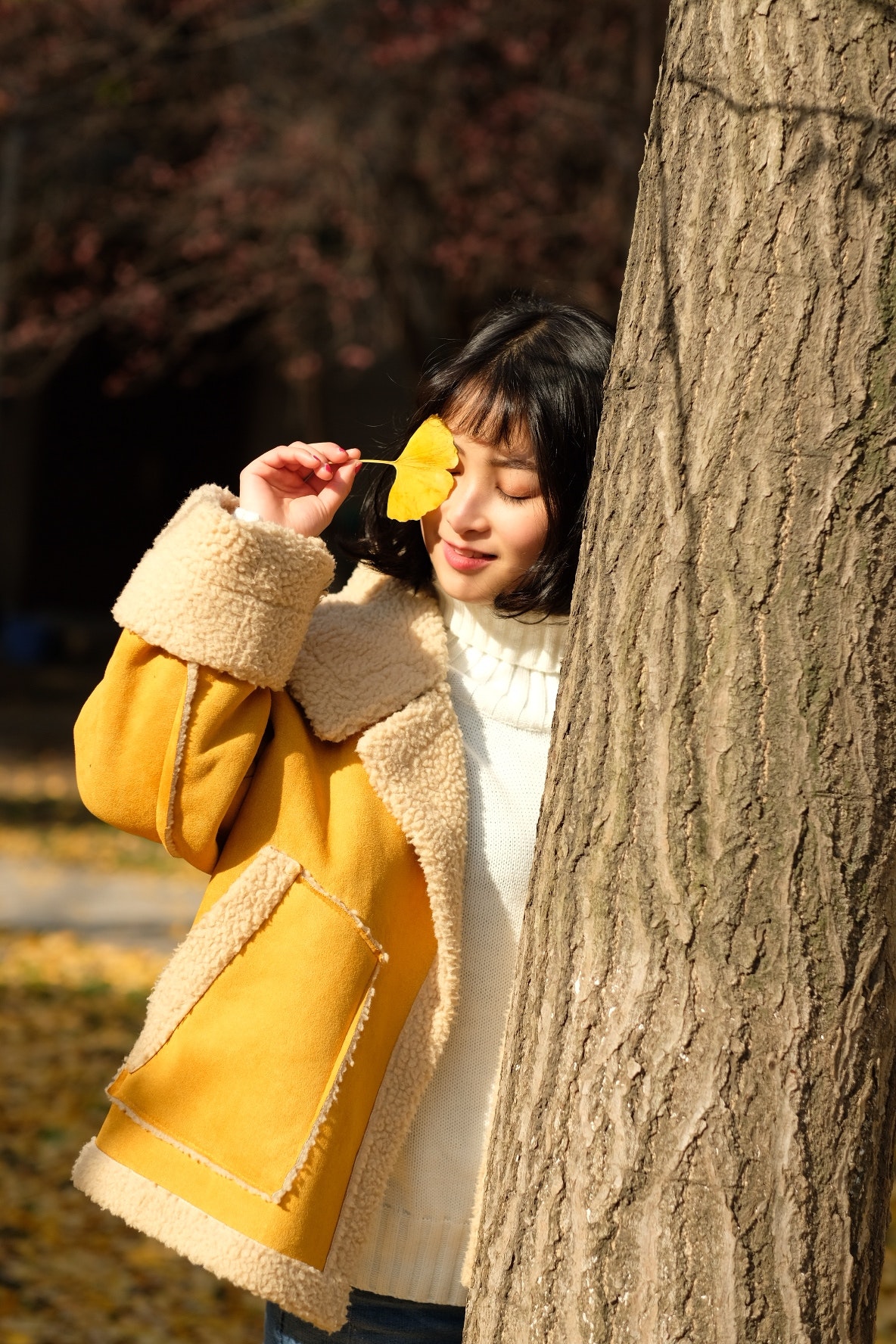Woman wearing yellow jacket holding yellow leaf photo