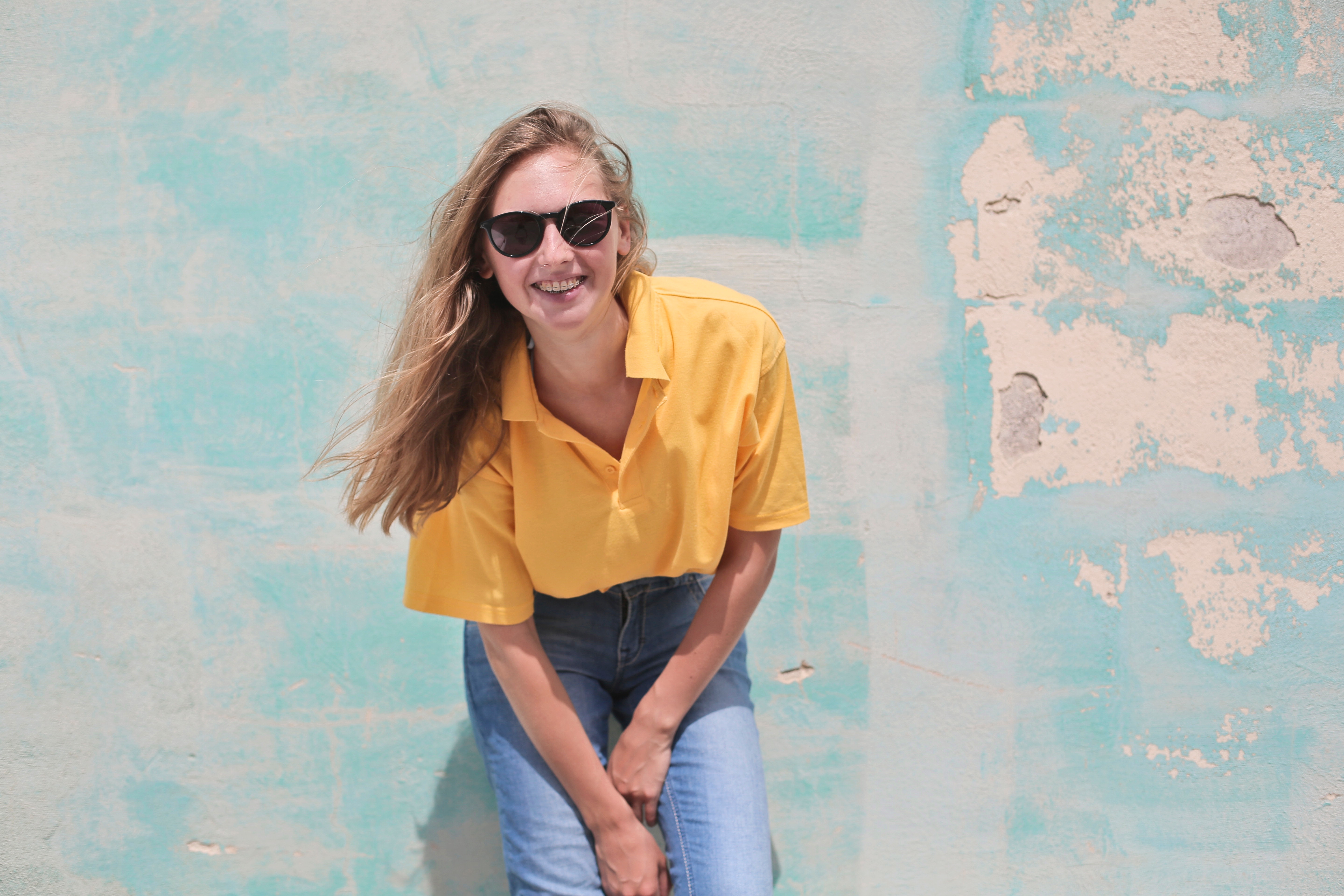 Woman wearing yellow polo shirt standing in front of teal concrete wall photo