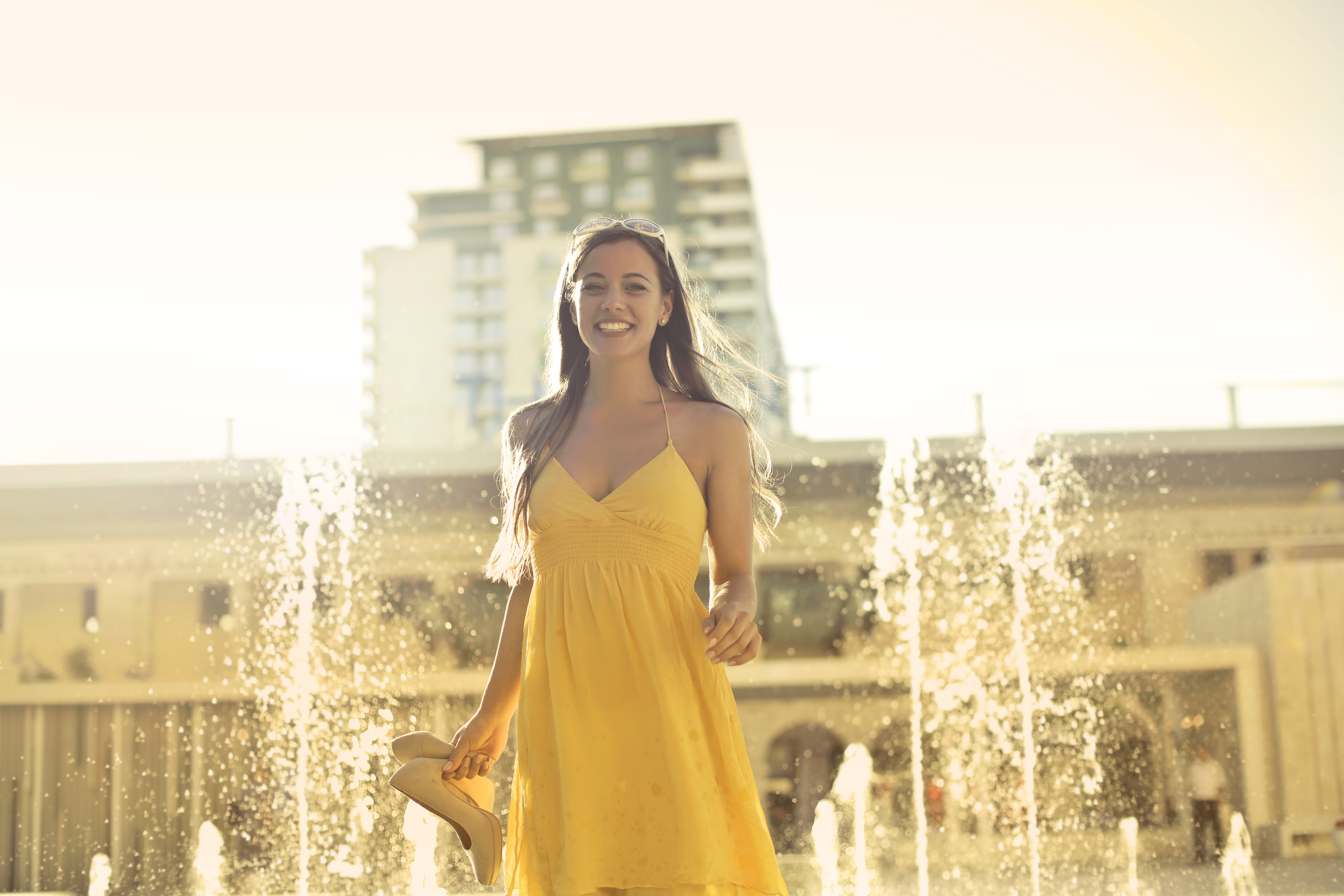 Woman wears yellow spaghetti strap dress stands near water fountain photo