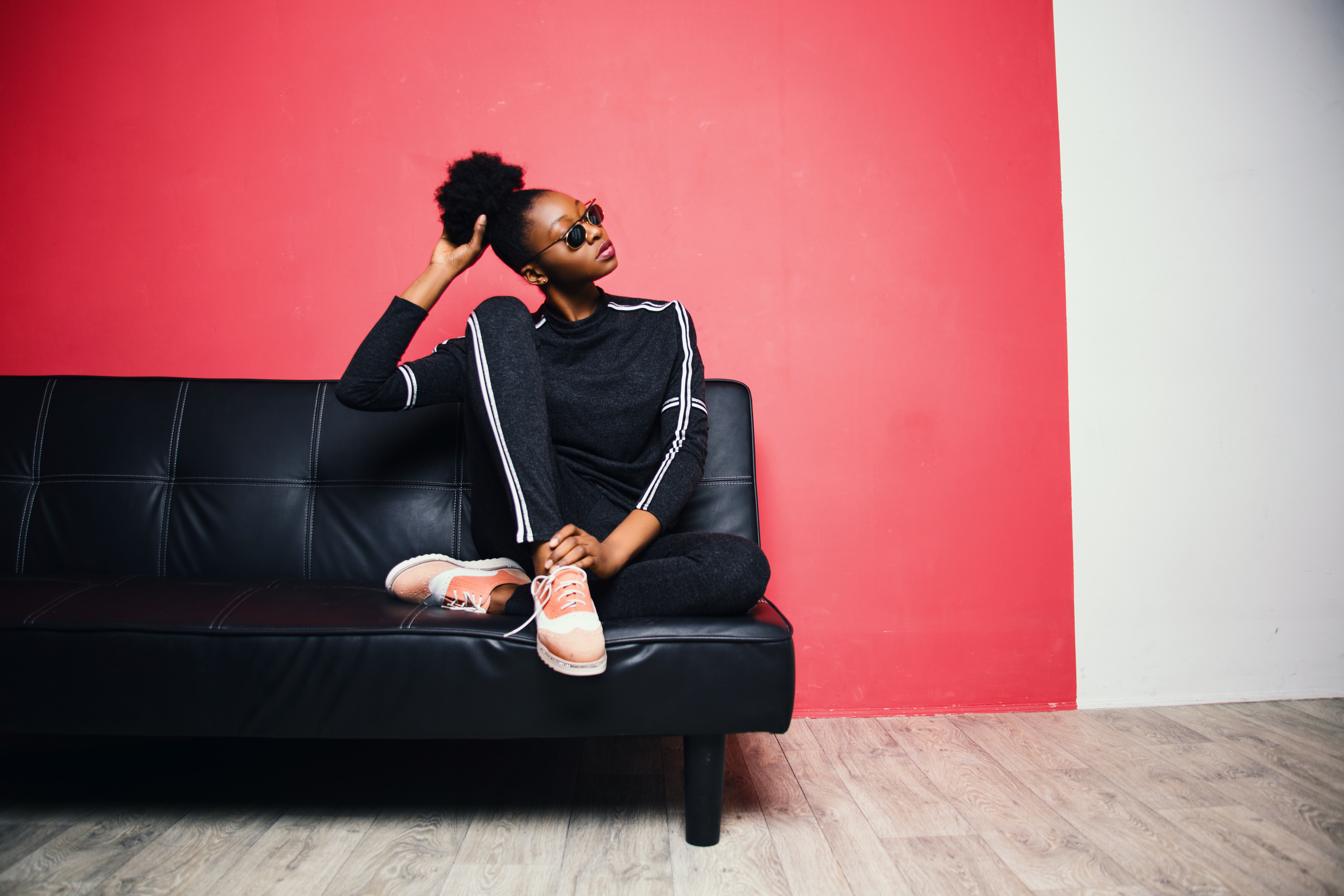Woman with black-and-white sweater with pants sitting on black leather sofa beside red painted wall photo