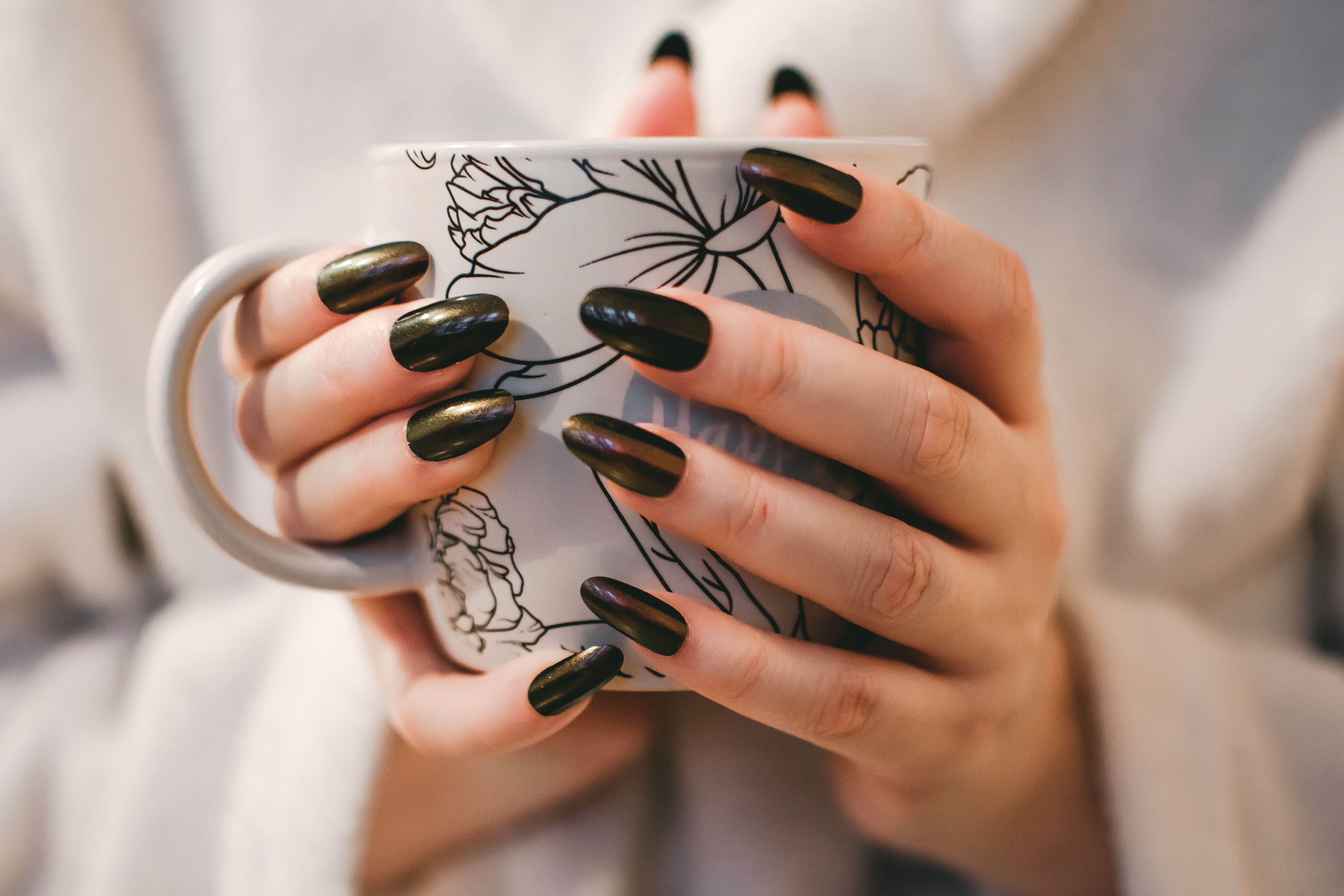 Woman with black manicure holding white and grey floral ceramic cup photo