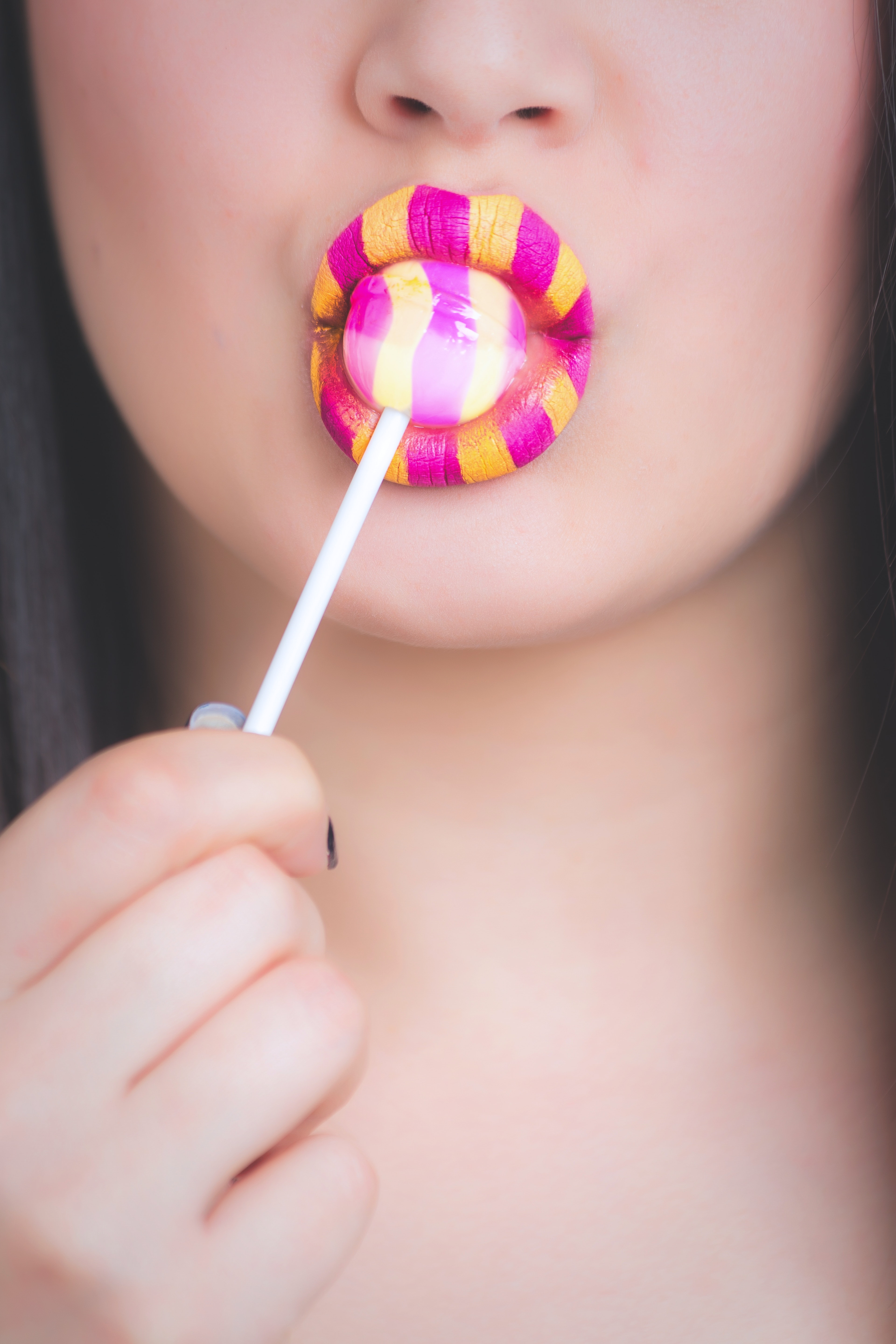 Woman with yellow and pink lipstick eating lollipop photo