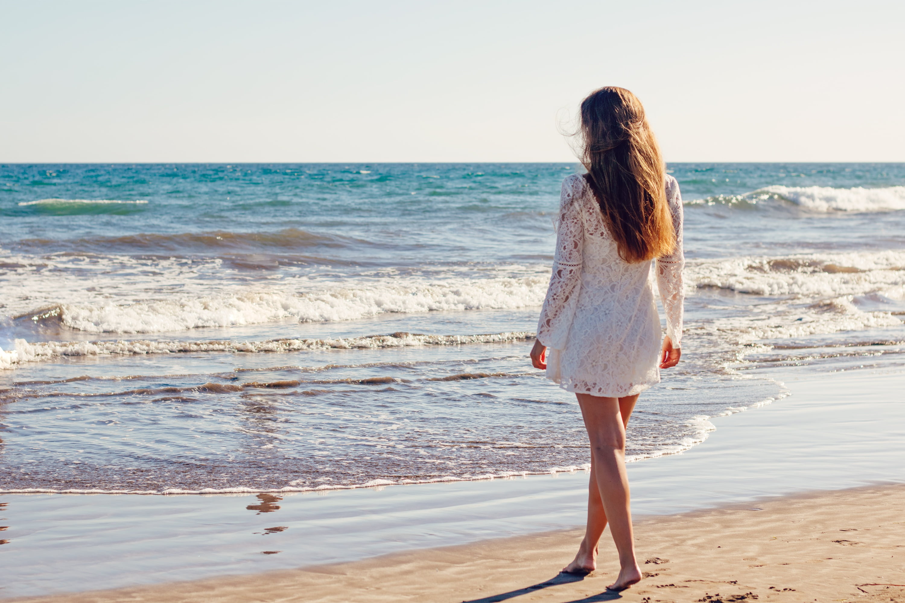 Woman wearing white long-sleeved dress standing near seashore on ...