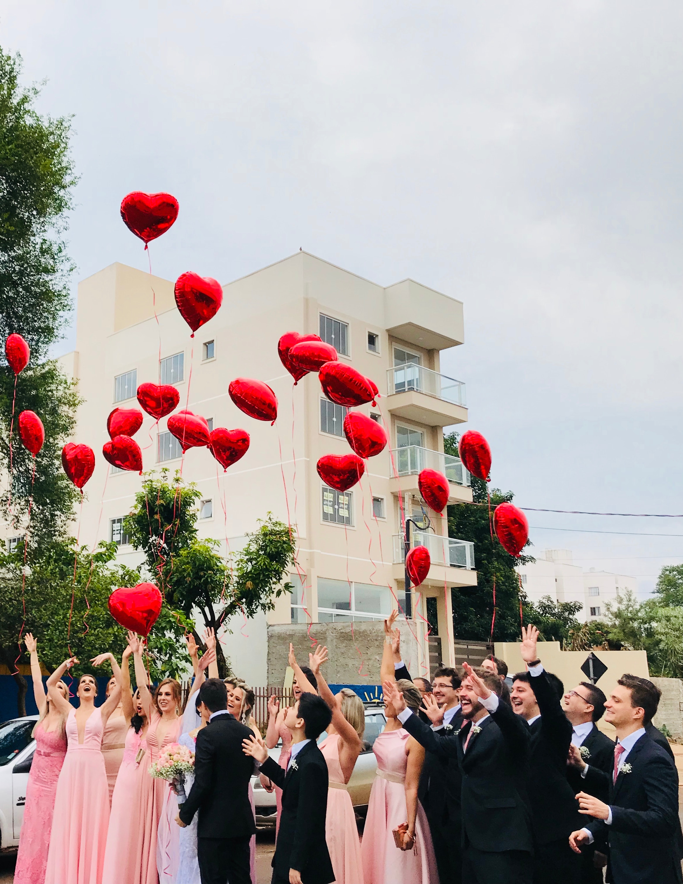 Women wearing pink dresses and men wearing black suit jacket and pants raising hands with red heart balloons photo