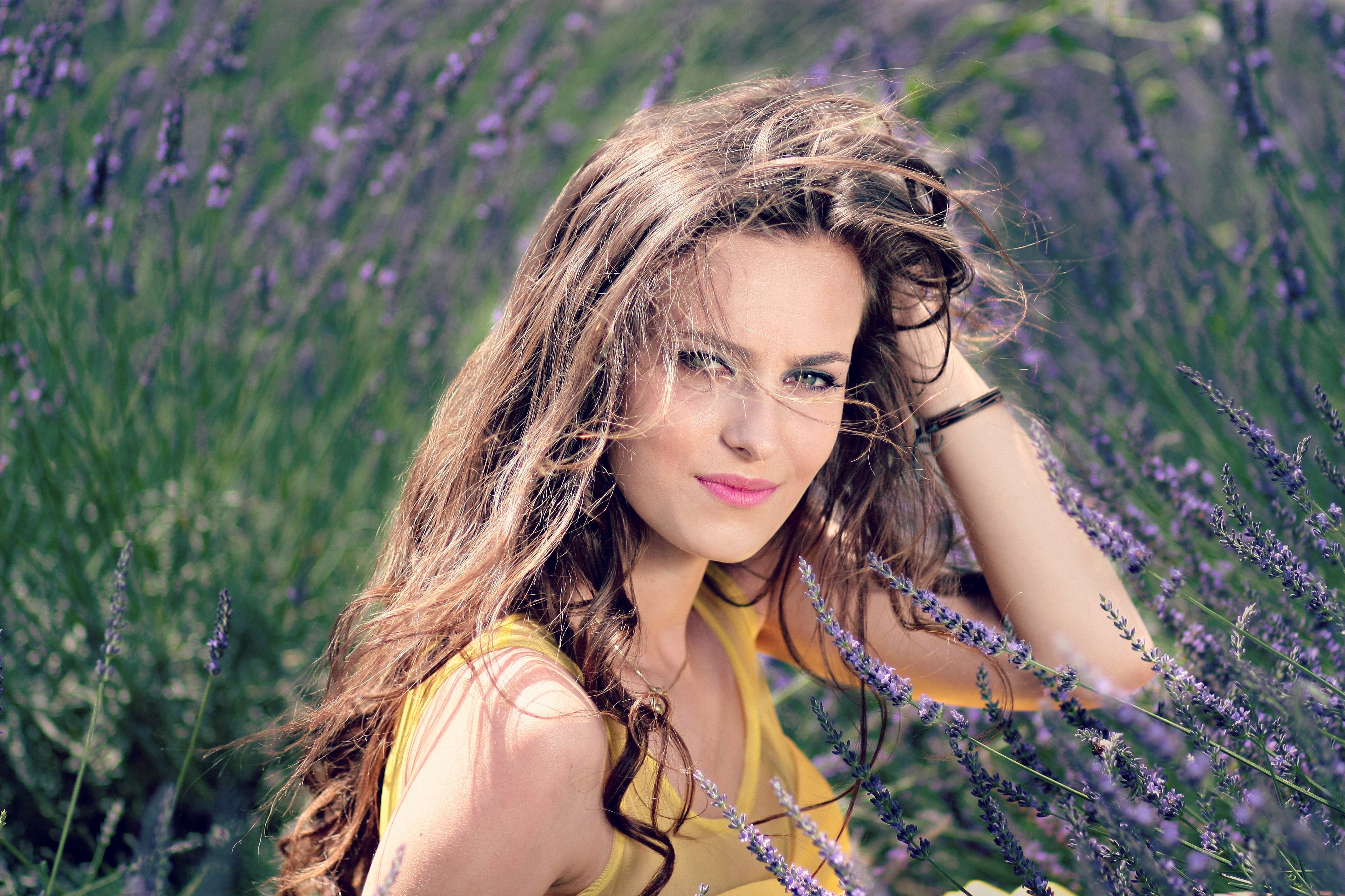 Women's yellow tank top holding her brown curly hair while sitting on a purple flower photo