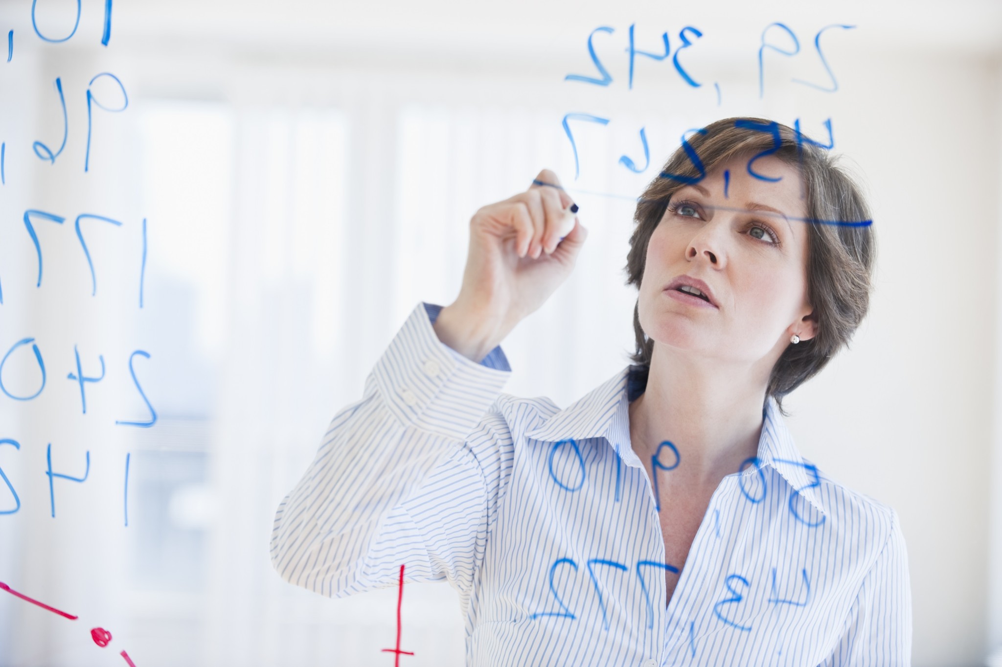 Mature businesswoman writing numbers on transparent glass wall - go ...