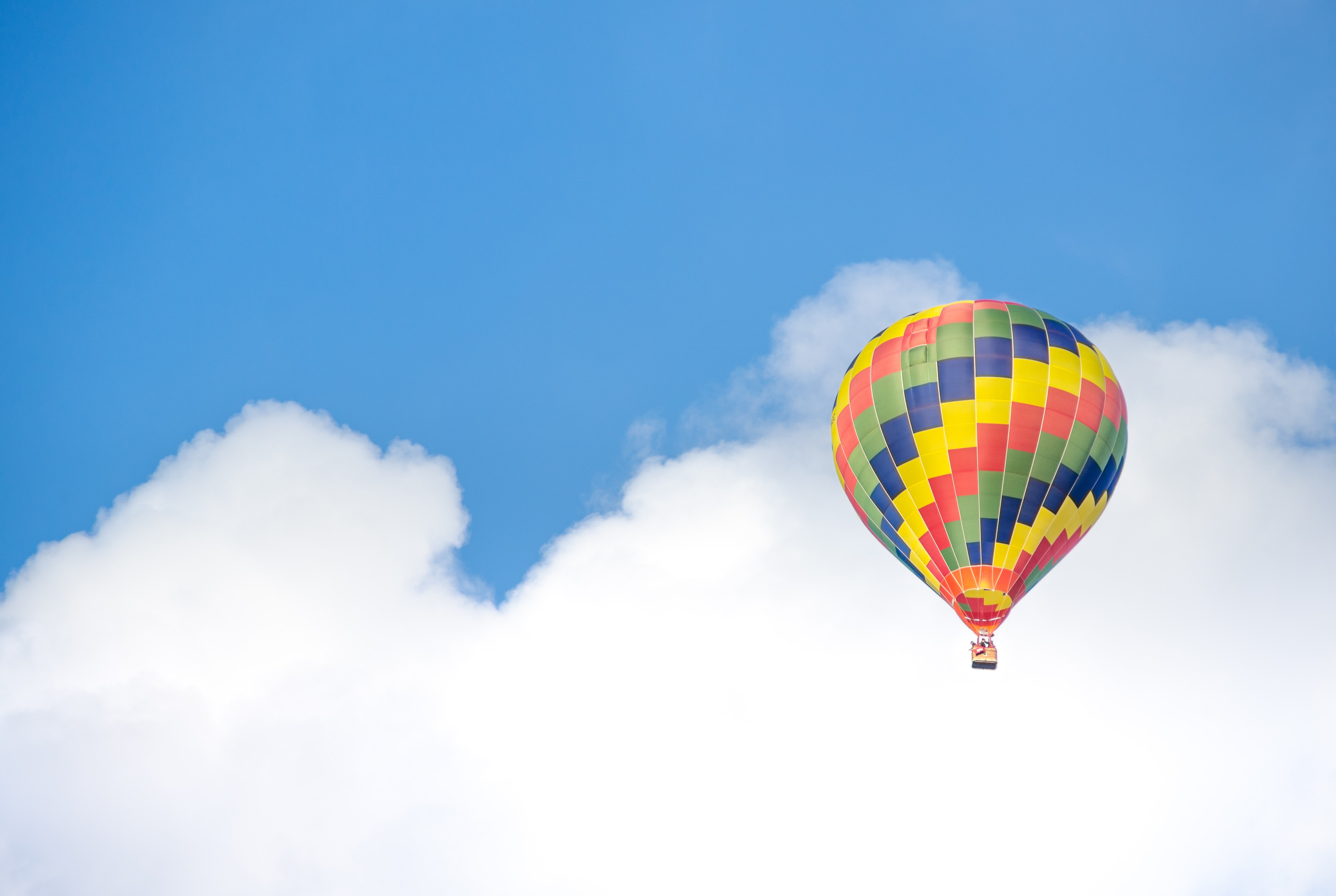 Yellow blue and green hot air balloon flying near white clouds photo