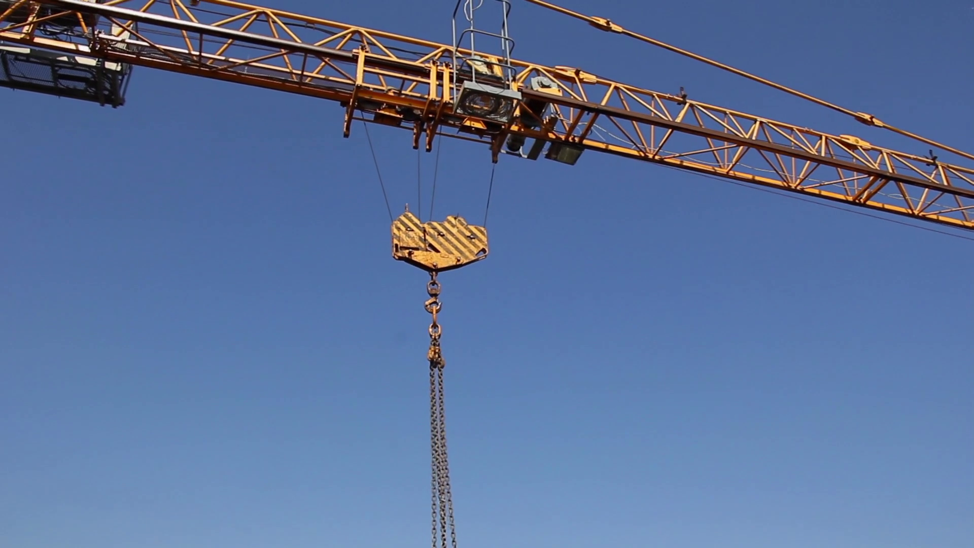 Yellow tower crane swinging iron chains slowly move on bright blue ...
