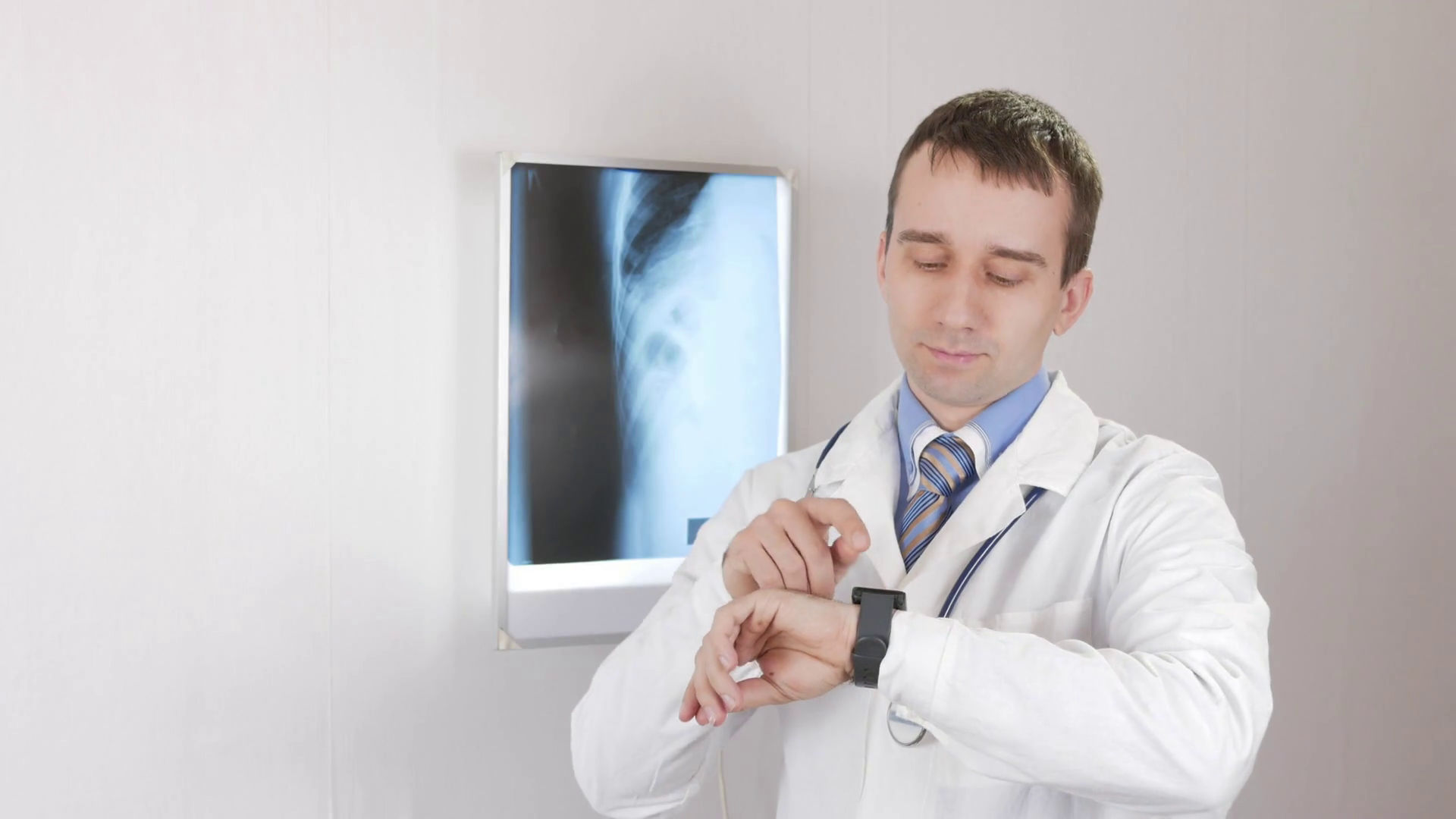 Young male doctor checks the messages on the smart watch. White wall ...