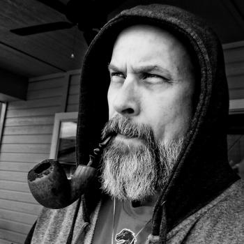 A brutal man with a beard smokes a pipe with tobacco