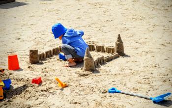 A child plays with sand, sculpting a sand castle on a sandy beach