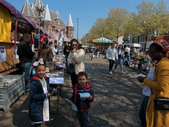 A small market wtih smiling children and mother, on the old city square Nieuwmarkt in Amsterdam downtown; free photo by Fons Heijnsbroek, 1 Mai 2022.