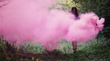 Beautiful girl in a forest runs through pink smoke from a color ...