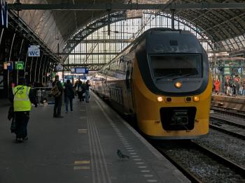 Central Station of Amsterdam city, with a yellow train on platform 1 and passangers and train conductor waiting to enter. Free Amsterdam photo by Fons Heijnsbroek, April 2022