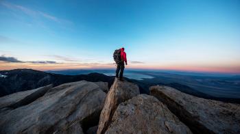 Strong mountain climber on the summit of a peak watching sunset ...