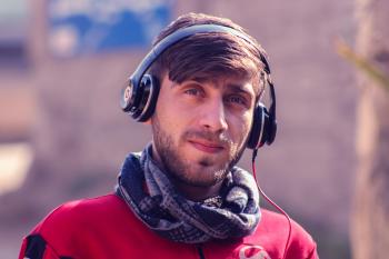 Closeup Photo of a Man Wearing Red Top, Gray Scarf, and Black Beats by Dr. Dre Headphones