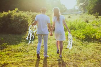 Coupe With White Dress and Suit Holding a White Dreamcatcher While Walking on Green Grass