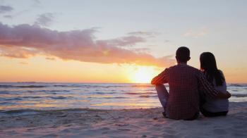 Young romantic couple sitting on the beach, admiring the sunset ...