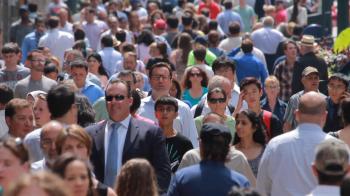 Telephoto shot with a backlit crowd of people on a wide sidewalk ...