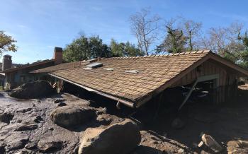 A damaged house is surrounded by large boulders & debris following ...