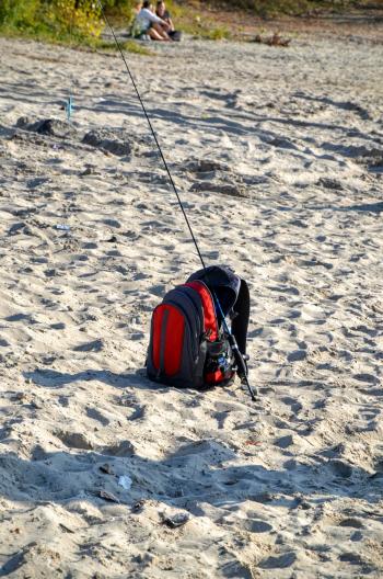 Fisherman's bag with spinning rod lies on the sand
