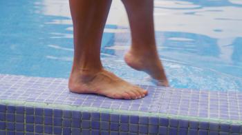 Closeup of feet walking by pool and dipping toe in water. Shot on ...