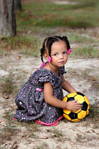 Girl in White Purple and Black Dress Holding Yellow and Black Soccer Ball Outside in Daytime