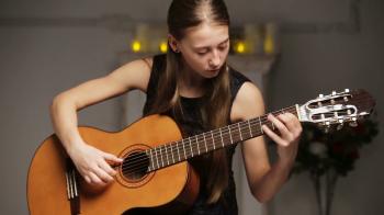 Young girl in black dress playing guitar sitting in front of a child ...