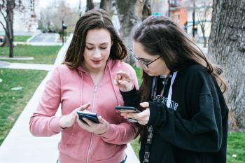 Girls show mobile photos to each other at the park