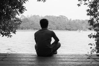 Gray Scale Photography of Man Sitting on Brown Wooden Floor Beside Body of Water