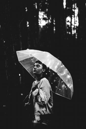 Grayscale Image of Woman Walking Through the Rain While Holding Umbrella